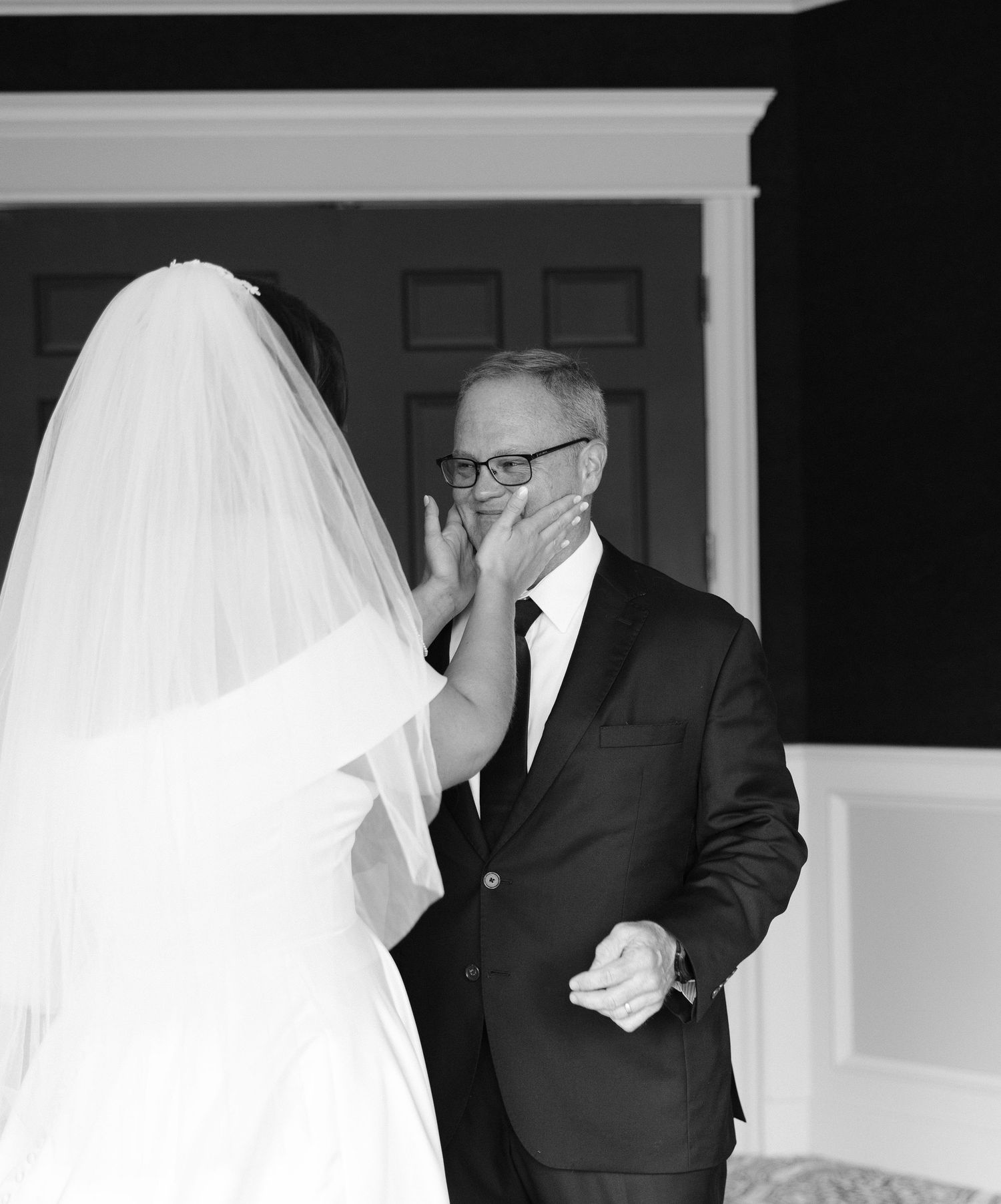 Black and white photo of emotional father covering his mouth seeing bride daughter in wedding dress for first look.
