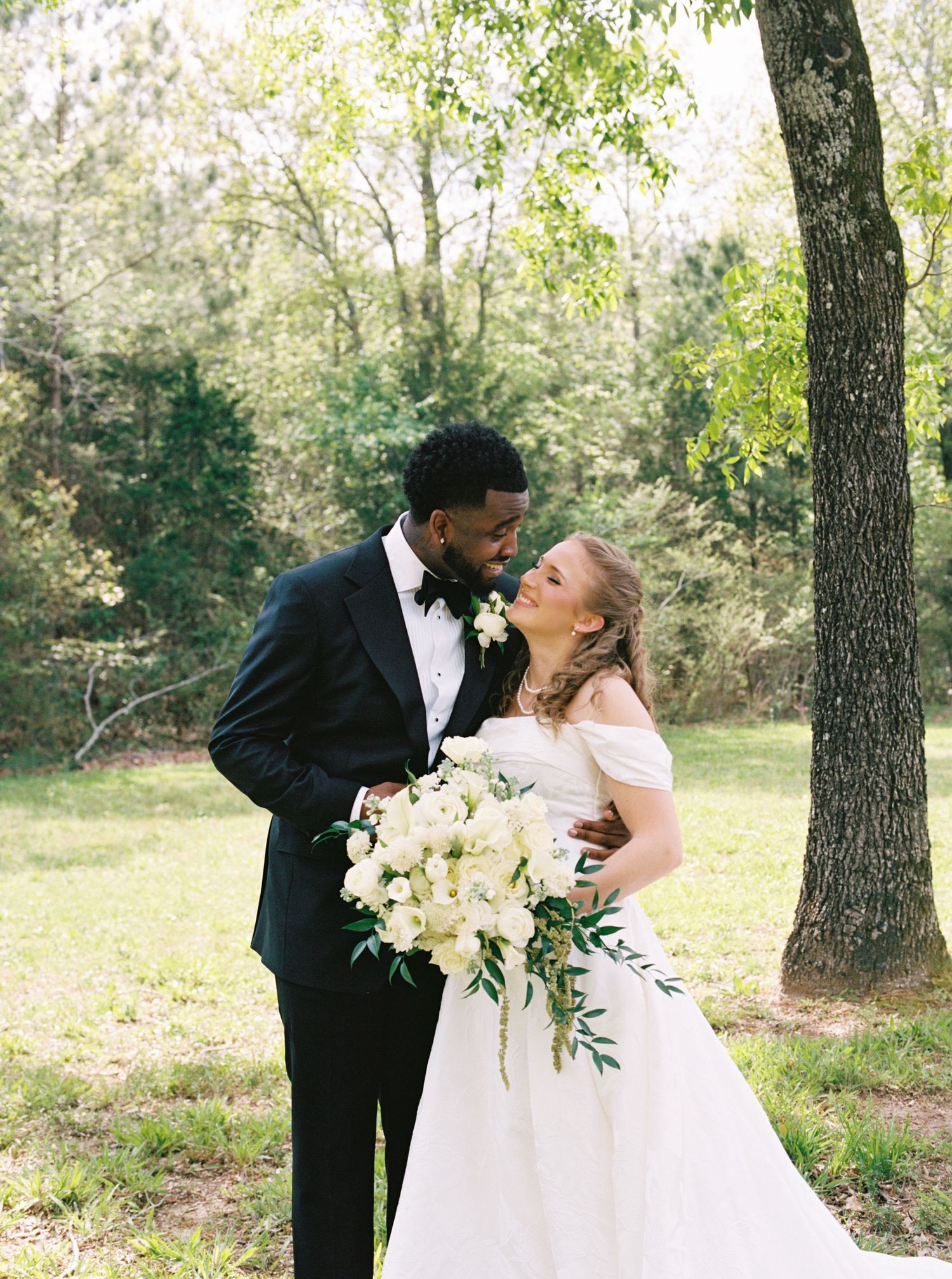 Bride and groom share romantic moment outdoors, bride holding large white floral bouquet.
