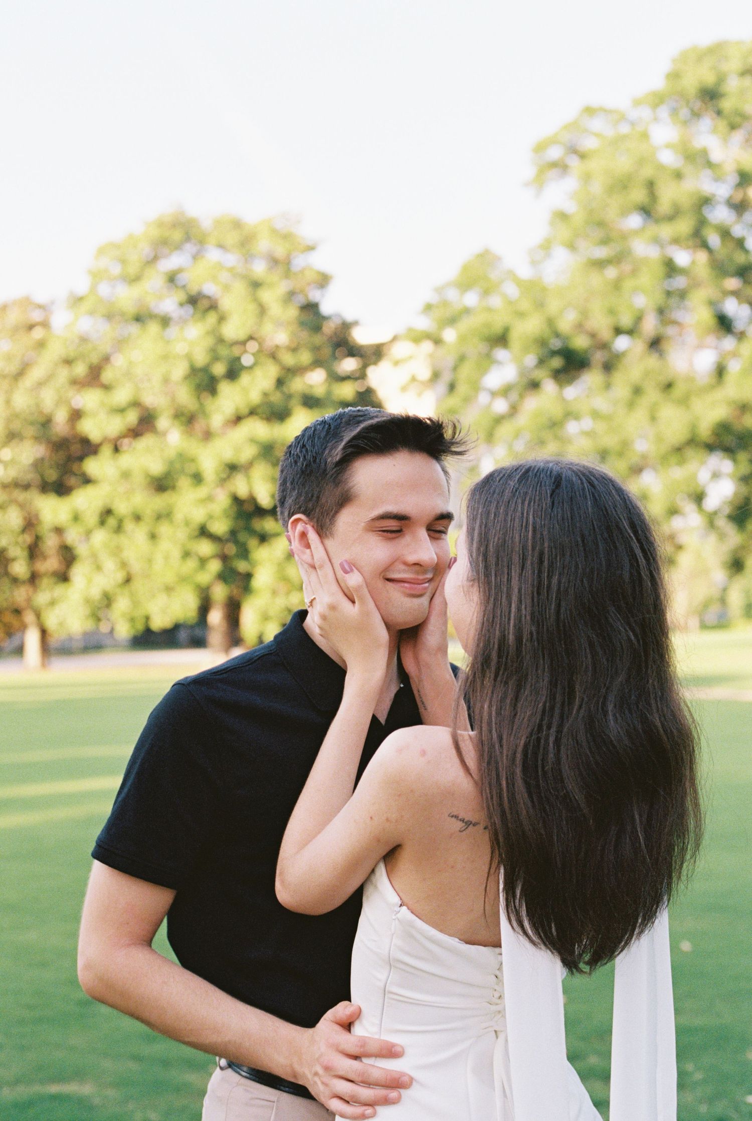Romantic couple embracing outdoors, woman in white dress tenderly touching mans face while he smiles.