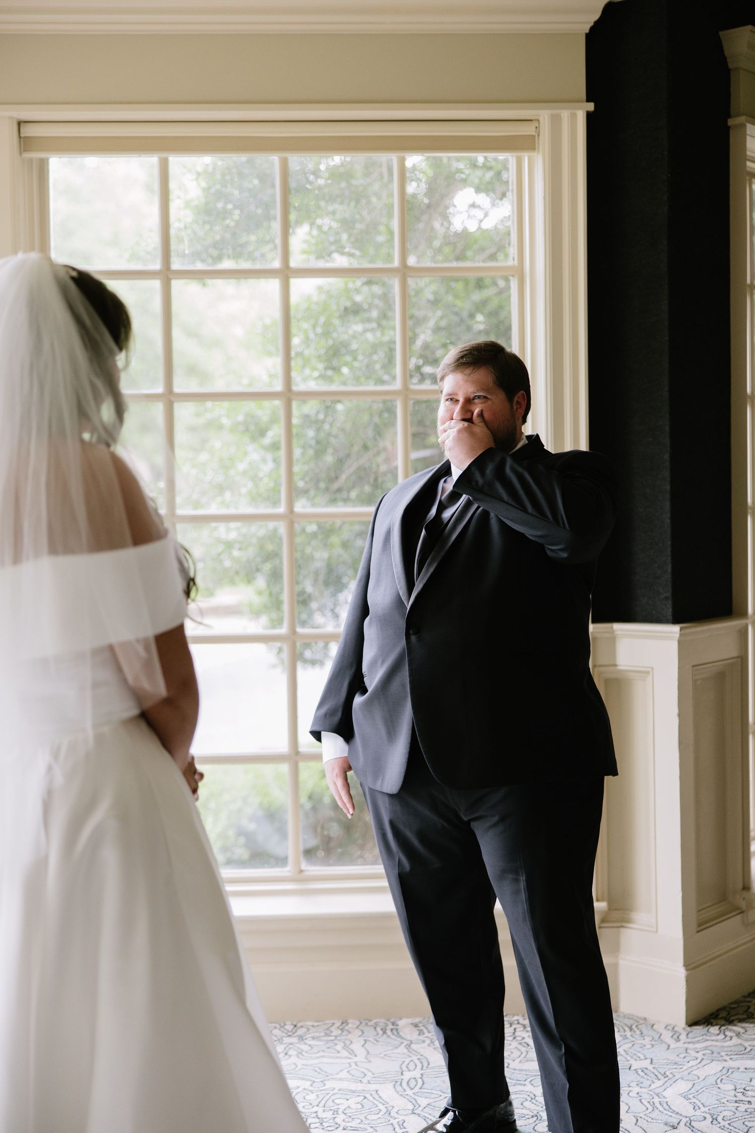 Emotional father sees his daughter in her wedding dress for the first time during a first look moment indoors.