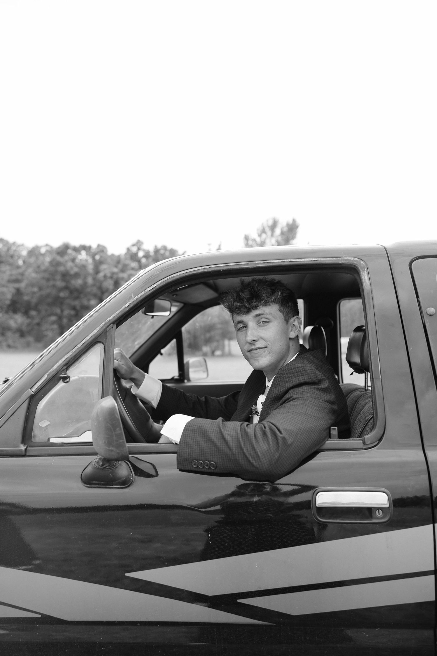 Young man in suit sitting in driver seat of truck, leaning out window, black and white photo.