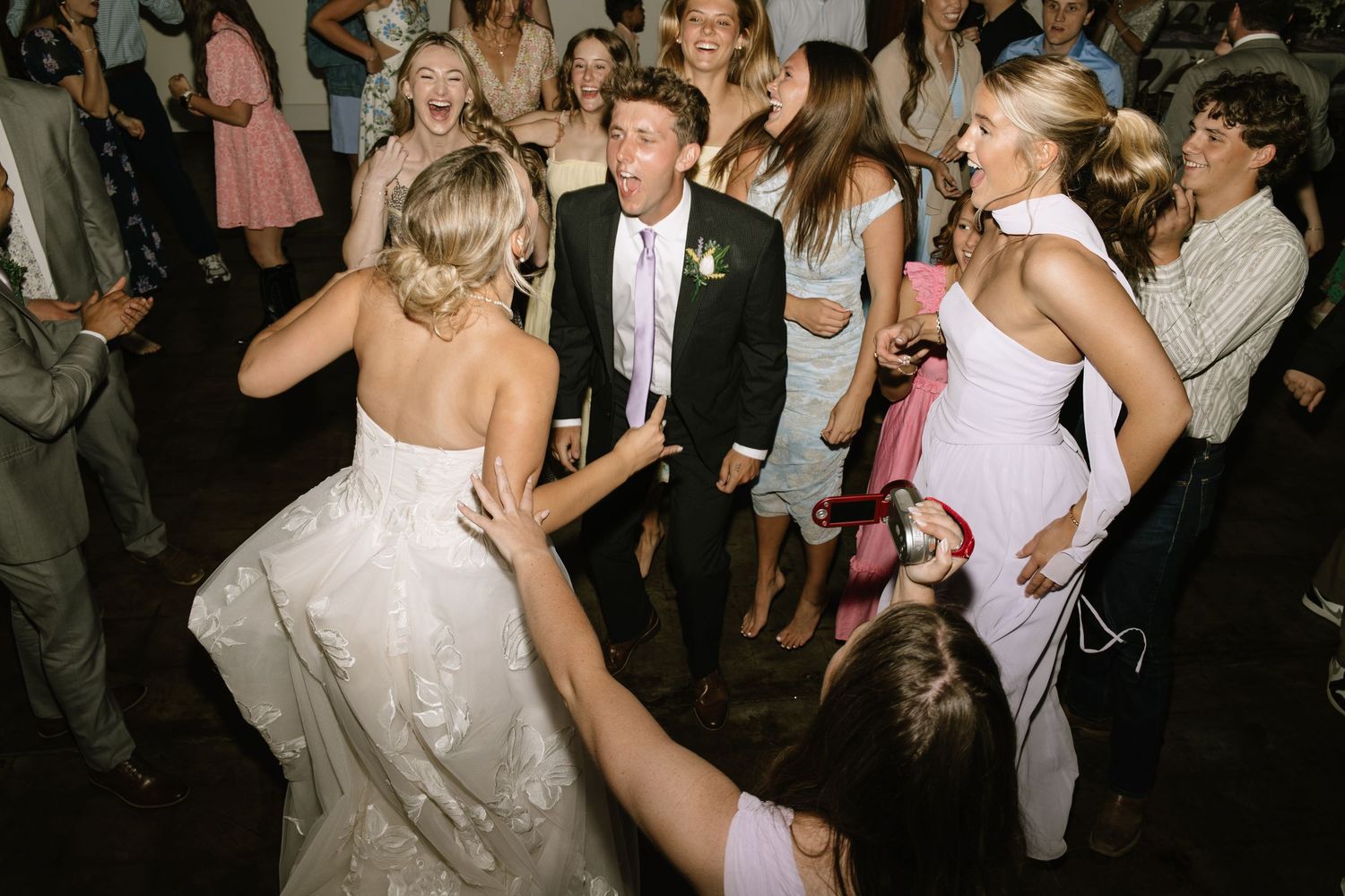 Bride and groom dancing joyfully with wedding guests on a lively reception dance floor.