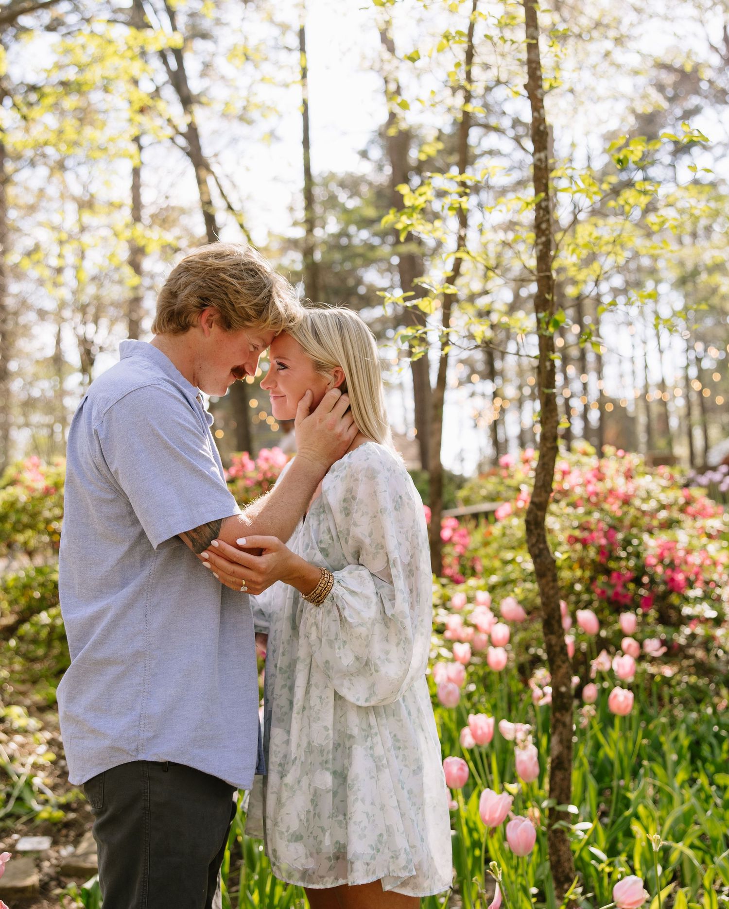 Romantic couple touching foreheads tenderly surrounded by pink tulips and spring blossoms.