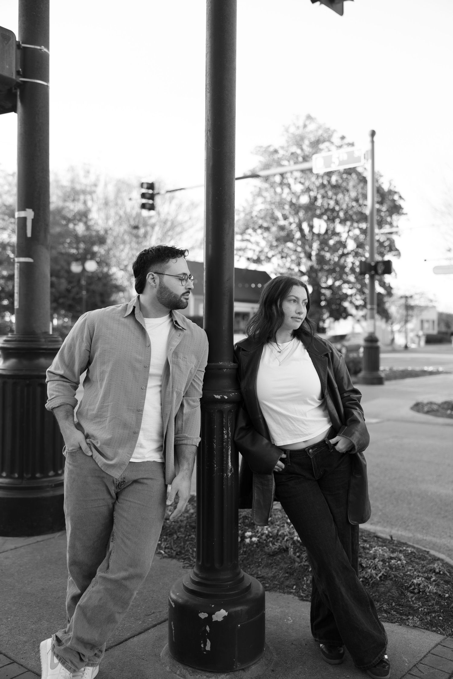Black and white photo of a man and woman leaning against a street lamp on an urban sidewalk.
