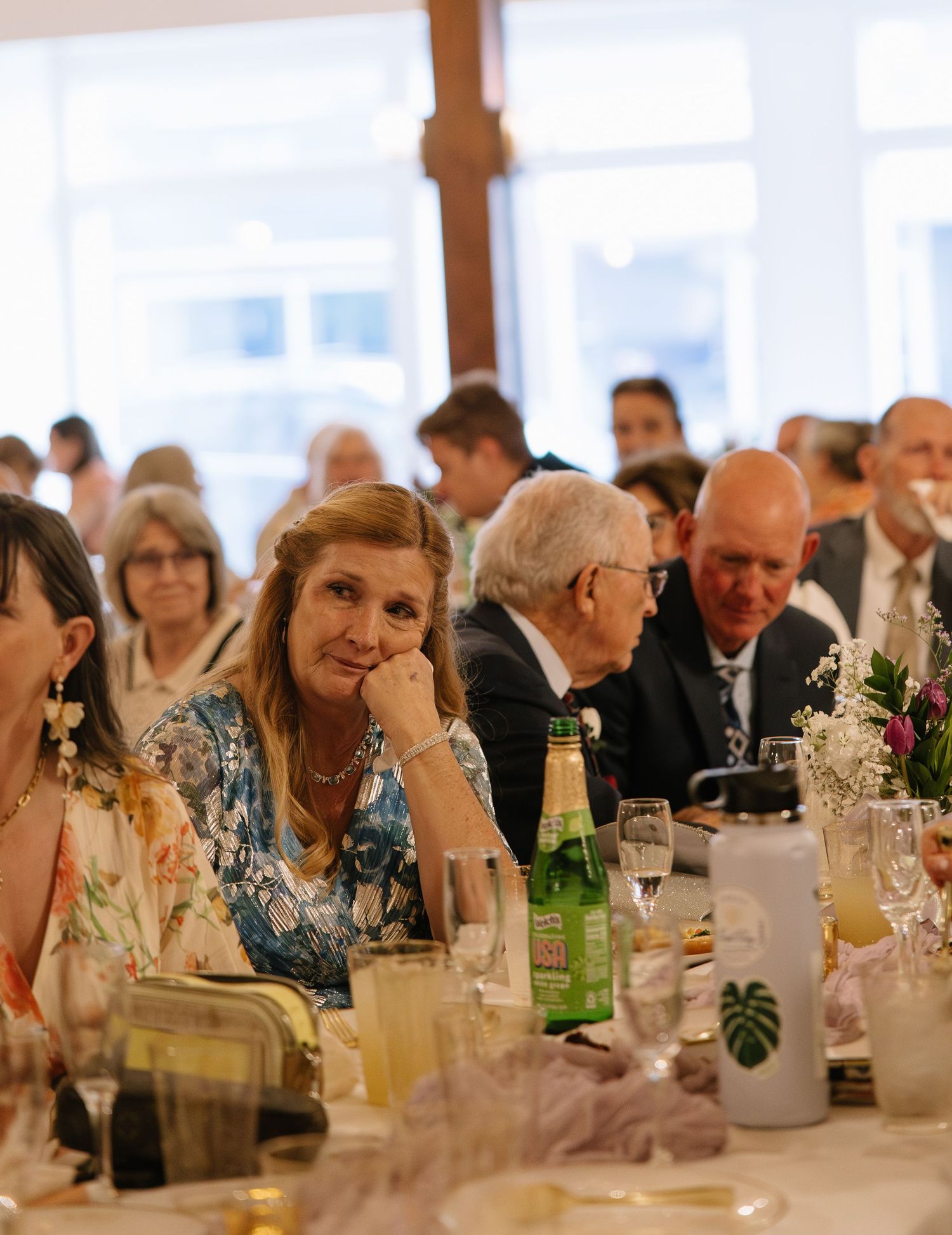 Guests seated at elegantly decorated tables during a formal wedding reception in a bright venue.