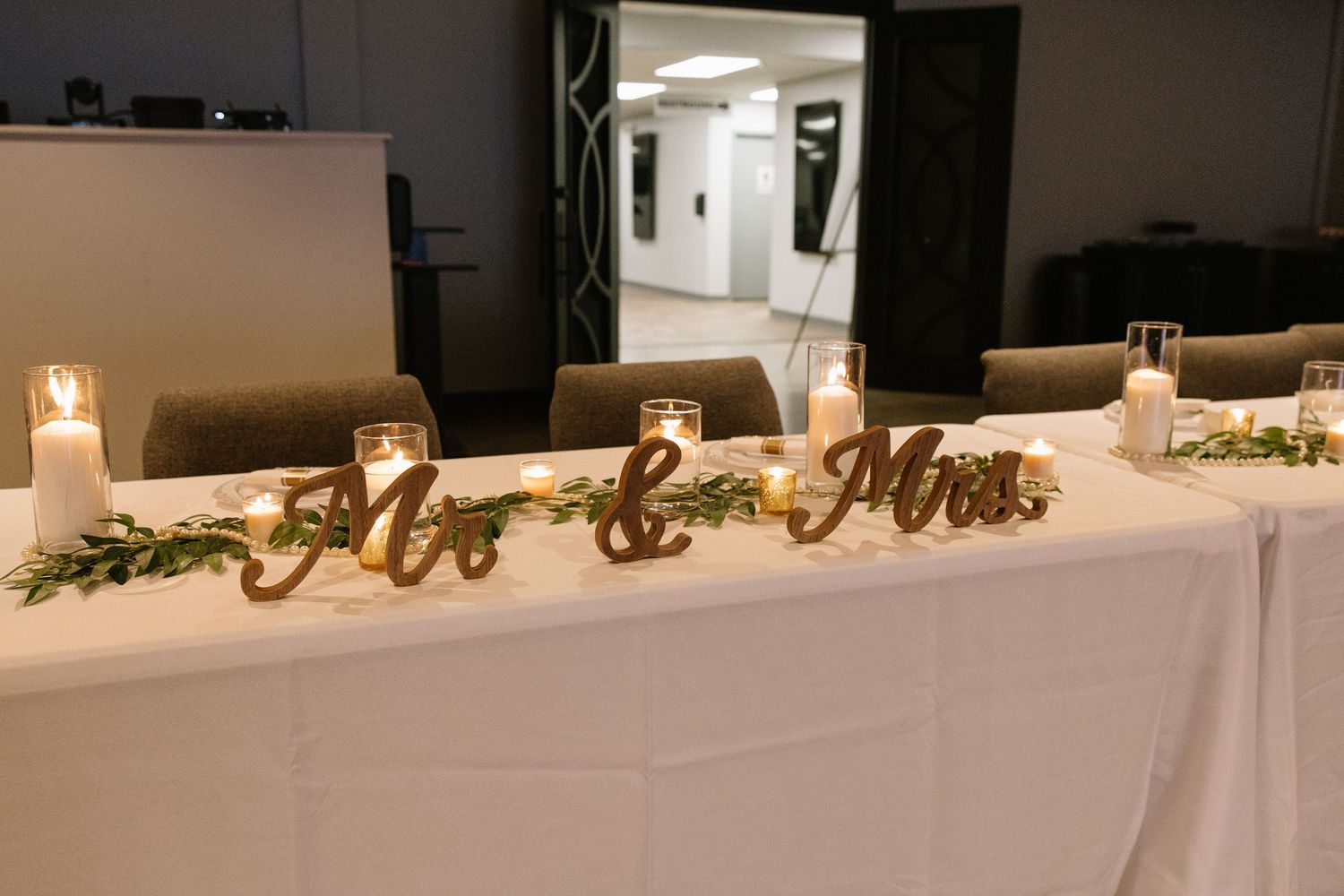 Elegant Mr. and Mrs. wooden signs on white tablecloth with candles and greenery at wedding reception.