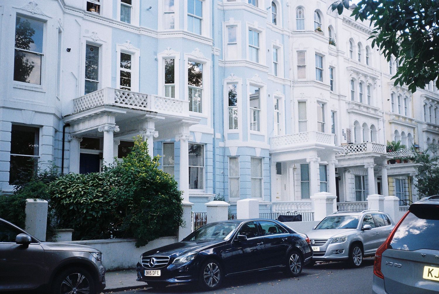 White Georgian townhouses with parked cars on a quiet street in Notting Hill, London.