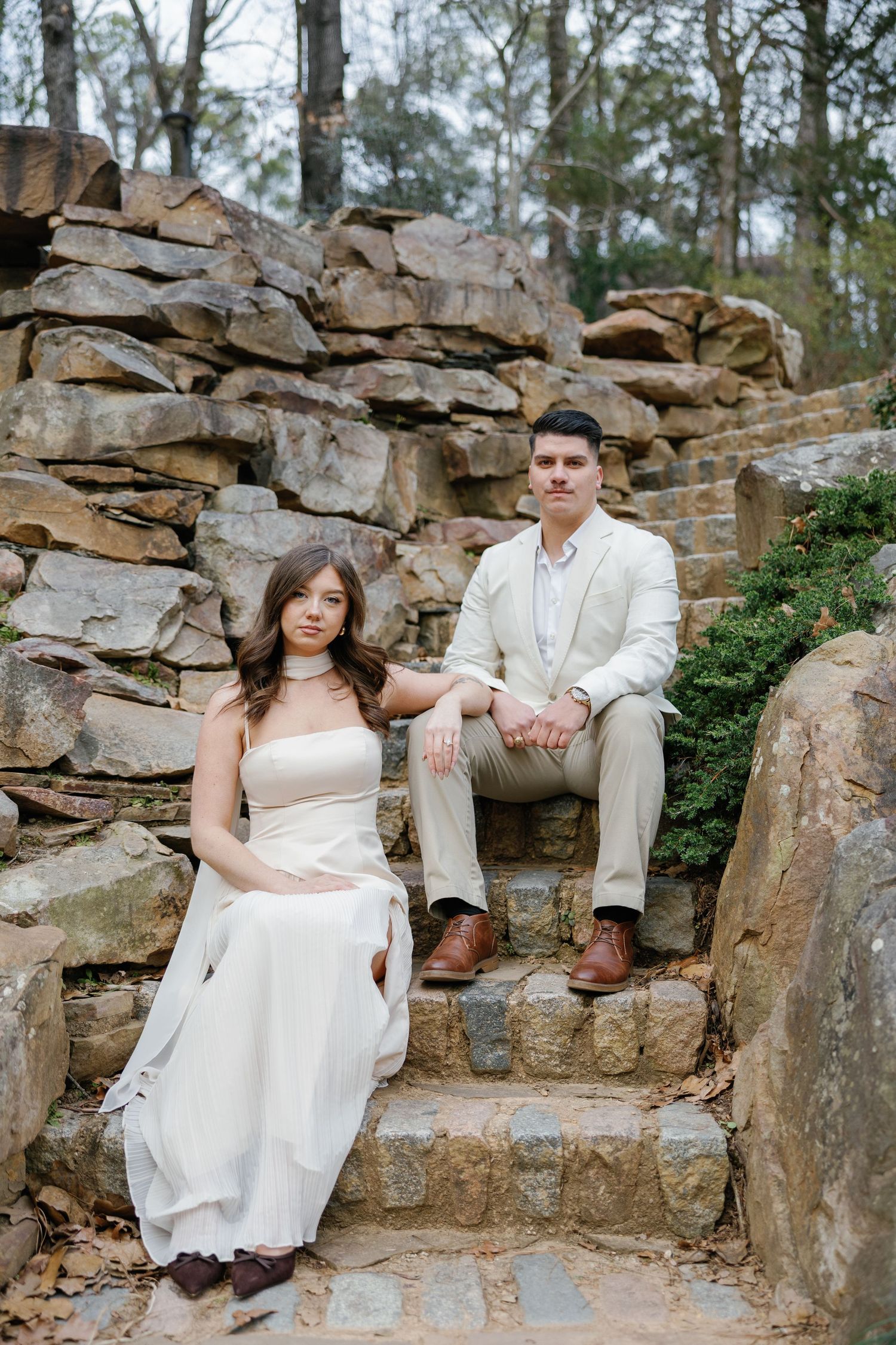 Couple in elegant white attire sitting on stone steps surrounded by natural rock formations outdoors.