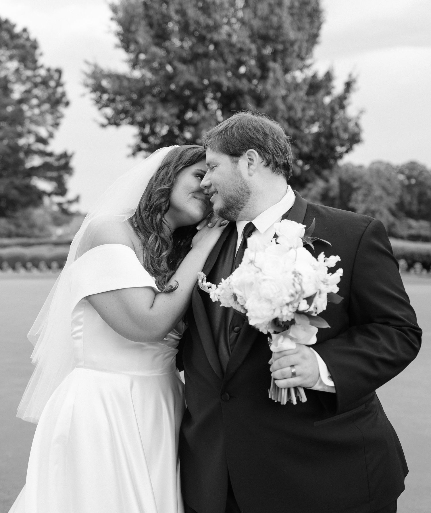 Black and white romantic photo of bride and groom sharing a tender nose-to-nose moment outdoors.