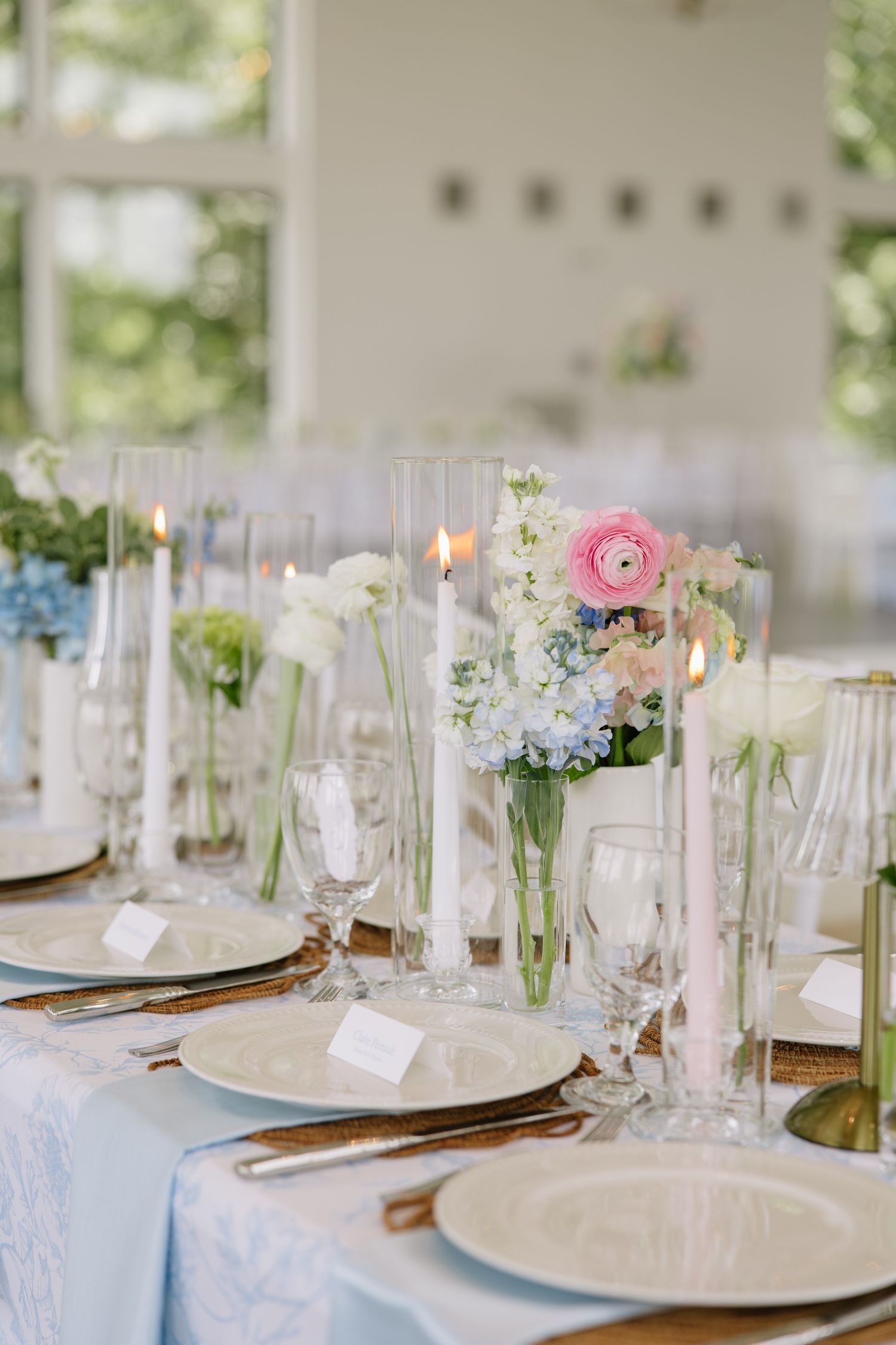 Elegant wedding reception table with blue linen, candles, and pink and white floral centerpieces in glass vases.