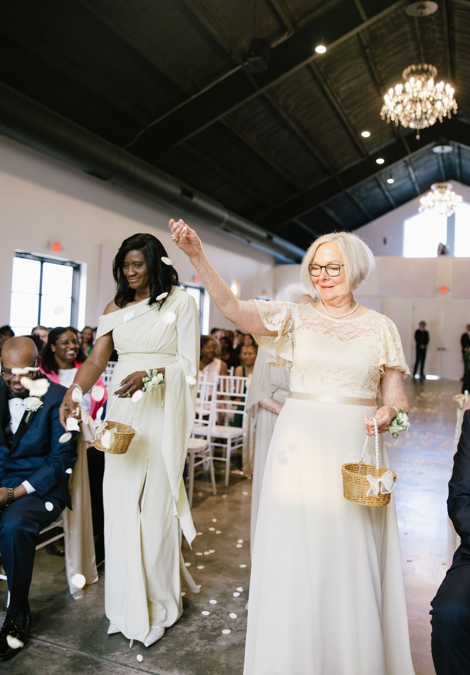 Two flower girls in white dresses joyfully walking down wedding ceremony aisle.