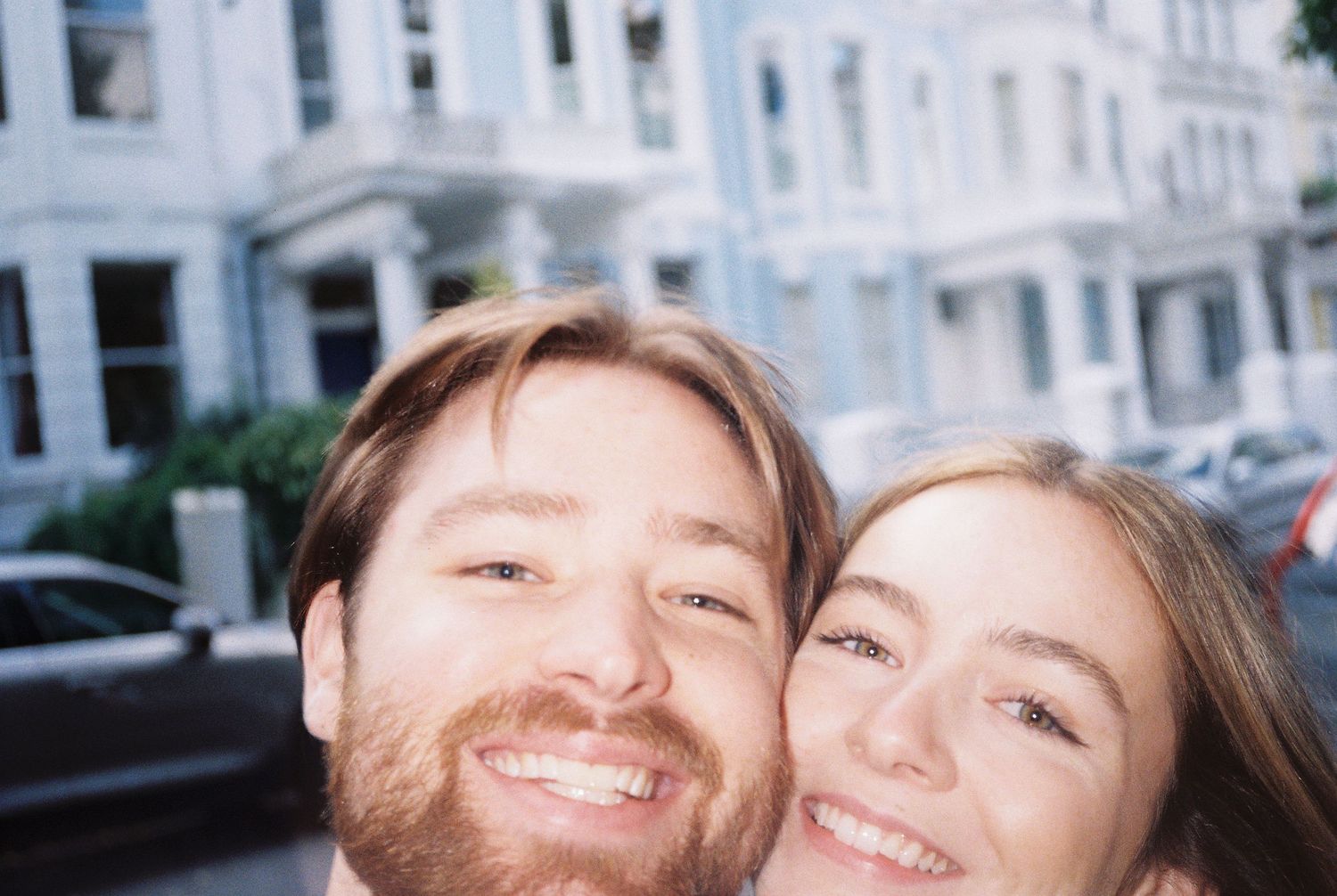 Happy couple taking a selfie on a street lined with colorful Victorian buildings.