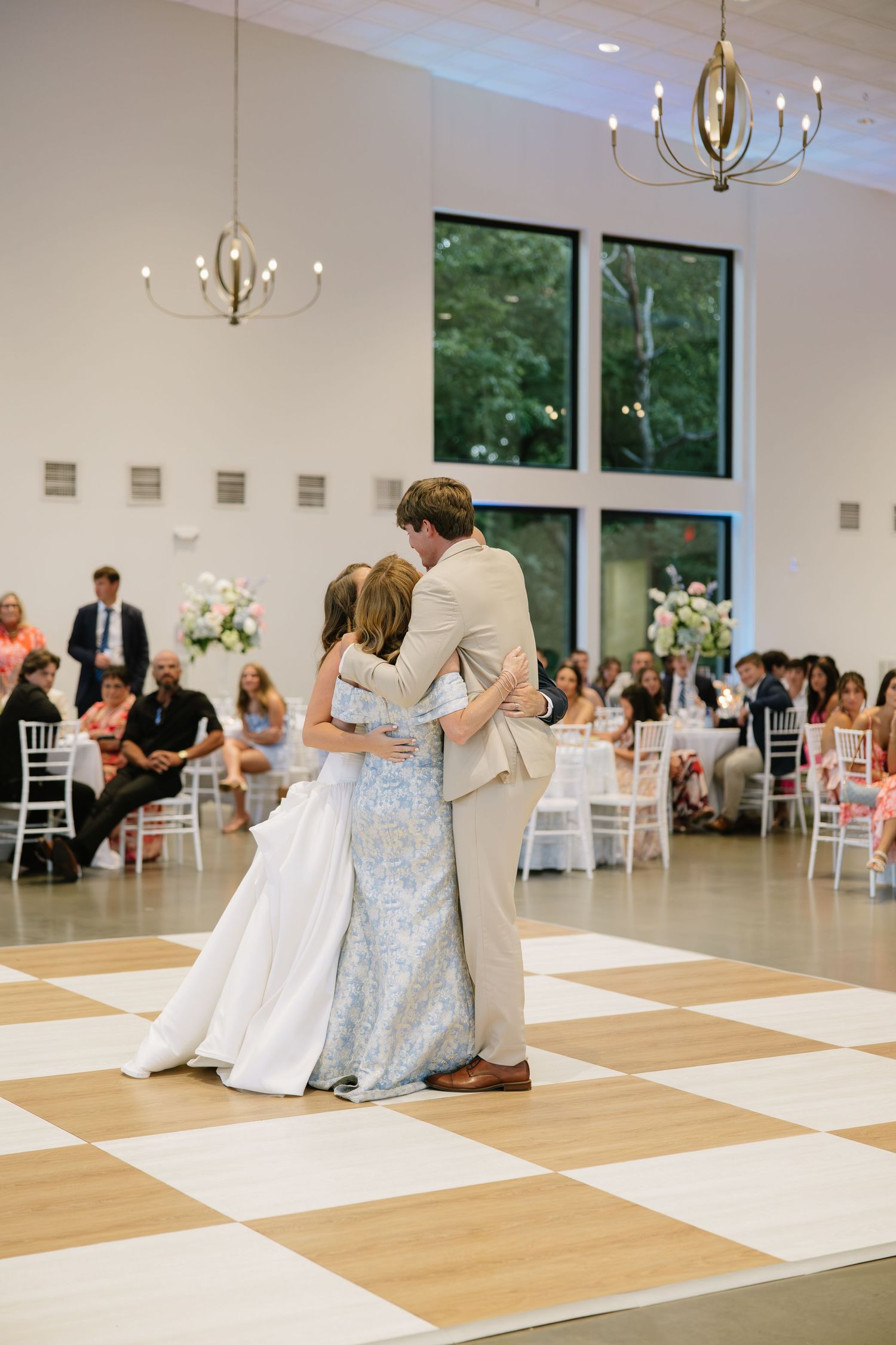 Couple sharing a tender first dance at wedding reception on checkered floor with guests seated nearby.