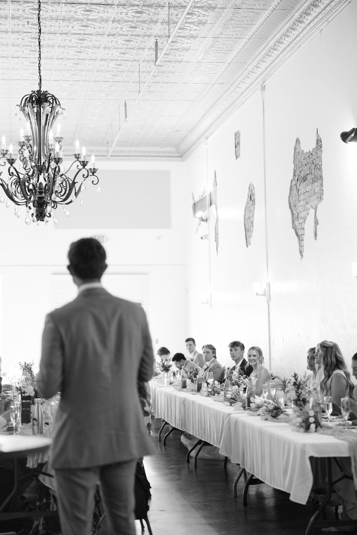 Black and white photo of wedding reception toast with guests seated at long decorated banquet table.