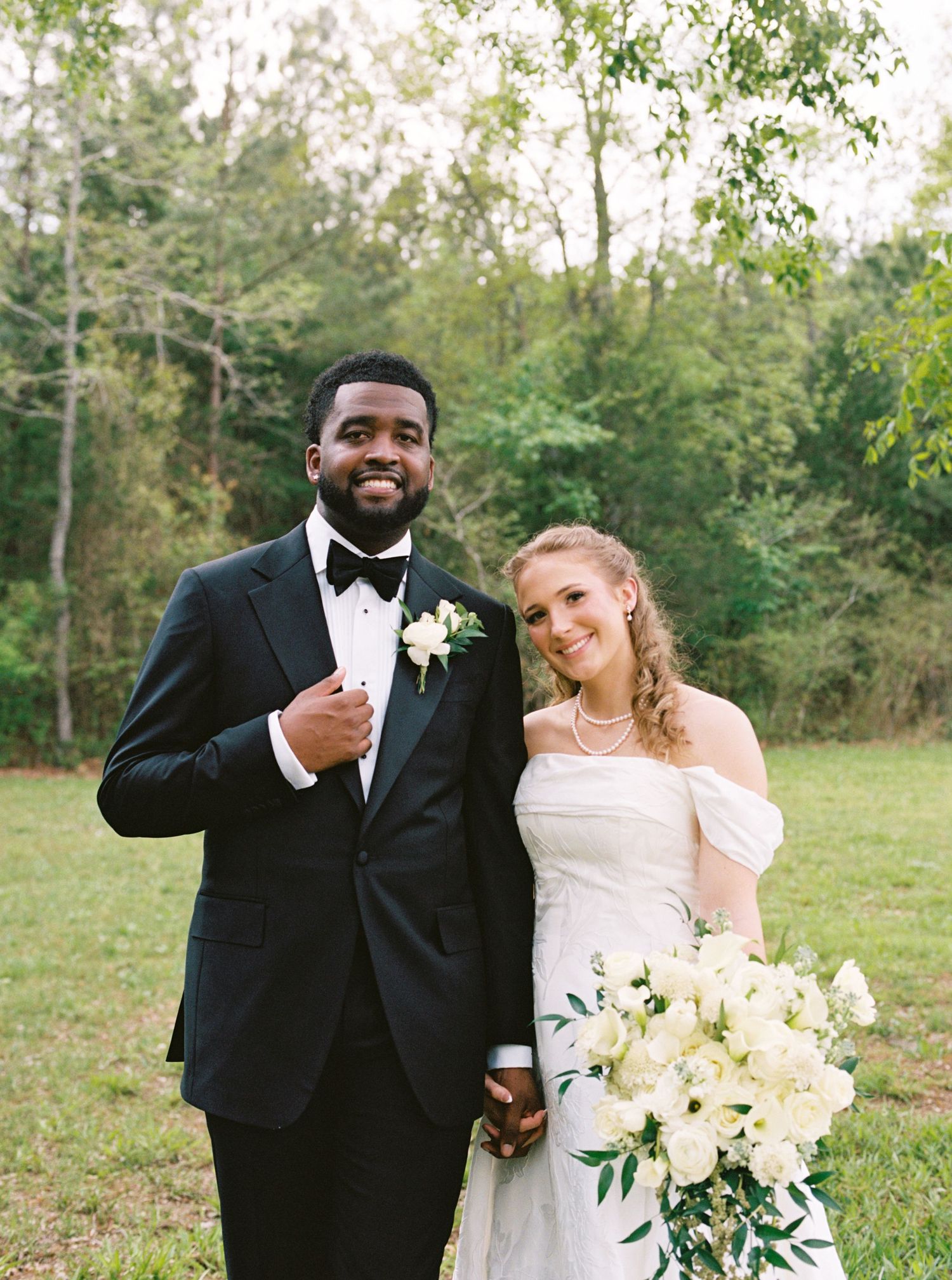 Happy interracial bride and groom smiling together outdoors in elegant wedding attire.