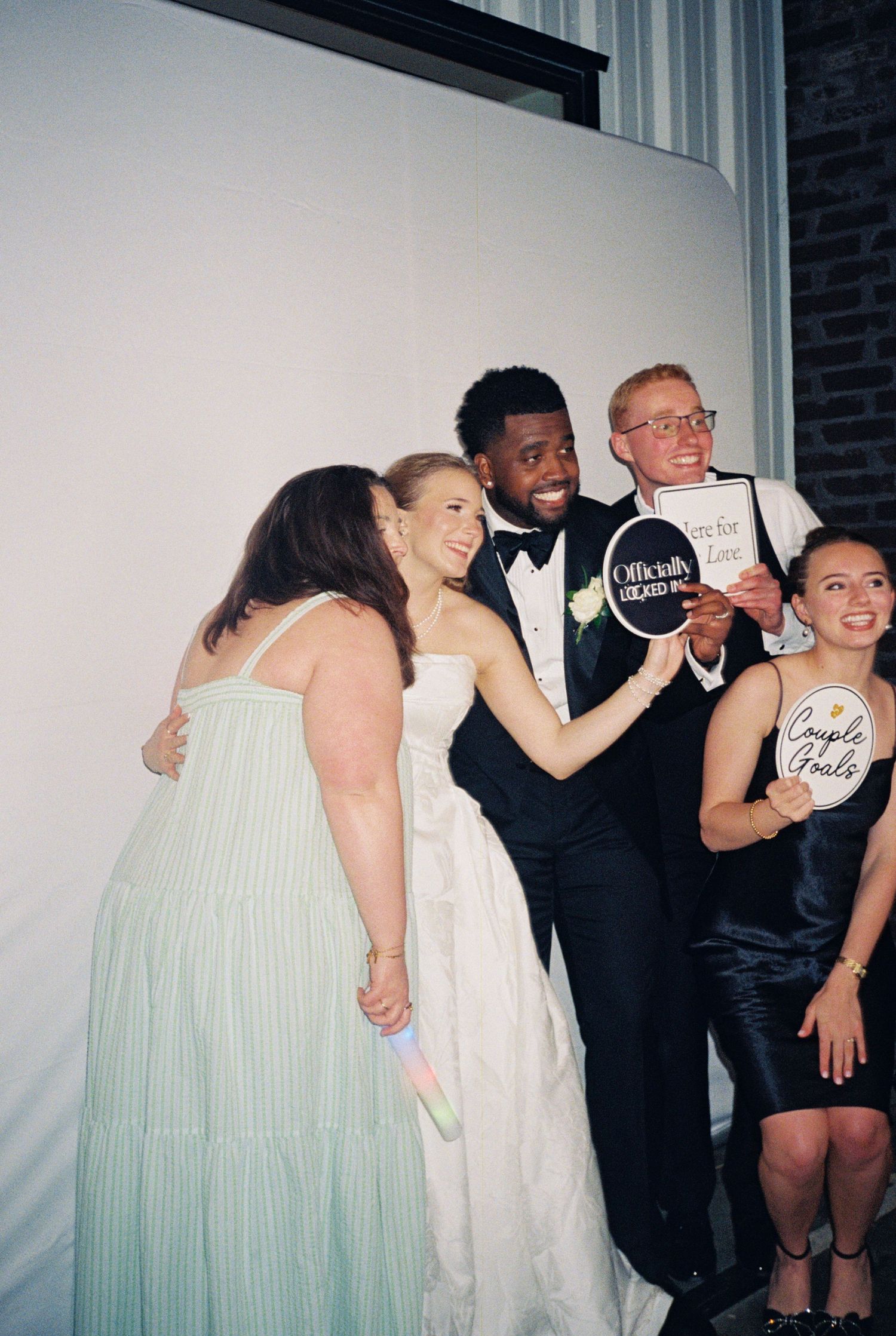 Wedding party group laughing and posing with fun signs at photo booth during reception.