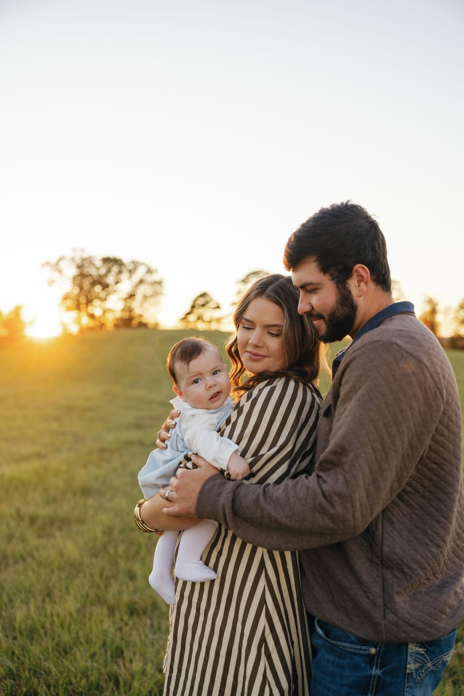 Happy young family with baby at golden hour sunset in green field.
