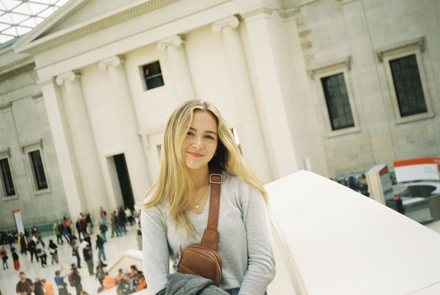 Young blonde woman sitting on a ledge inside a grand museum atrium smiling at the camera.