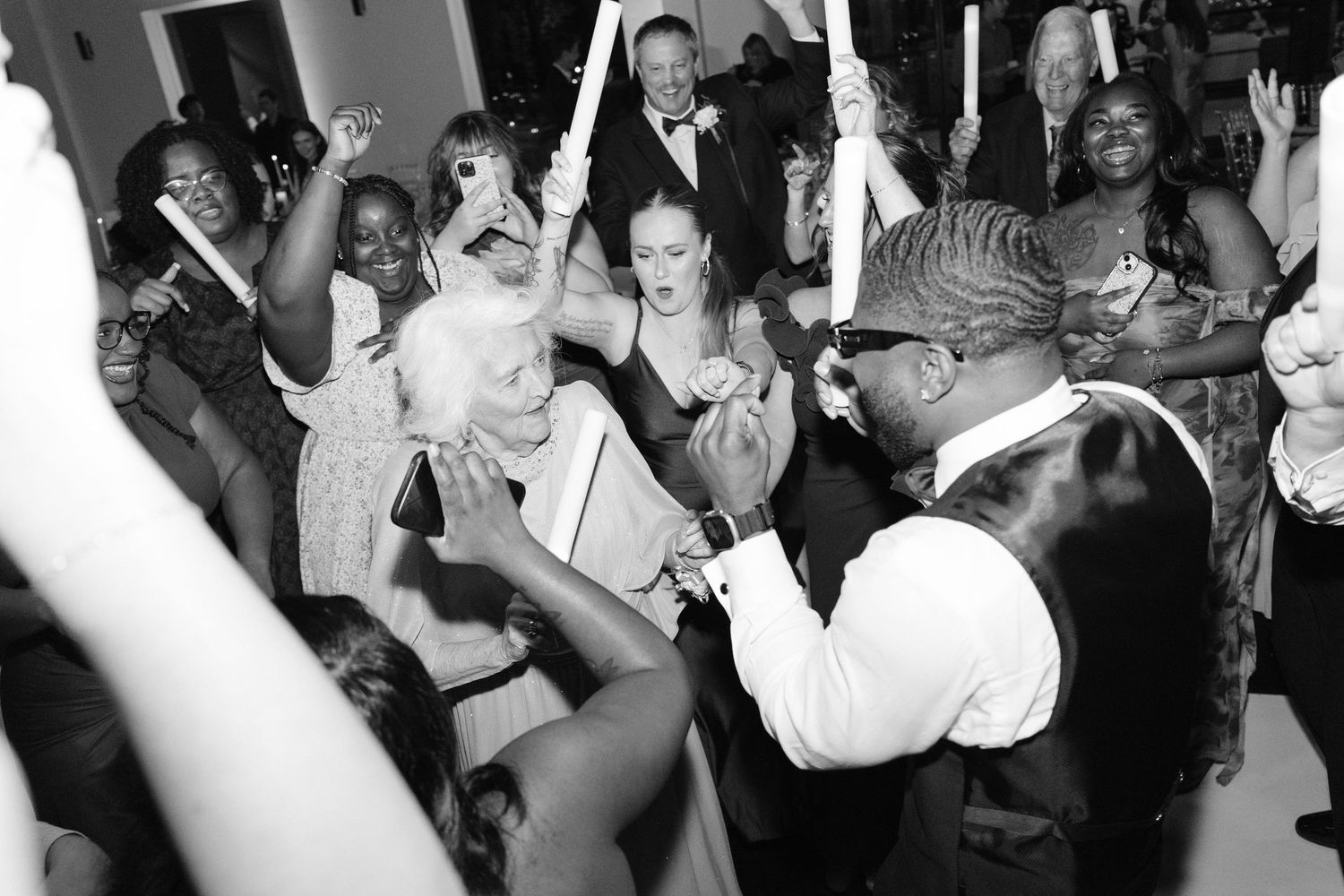 Black and white photo of wedding guests dancing and celebrating with the groom at a lively reception party.