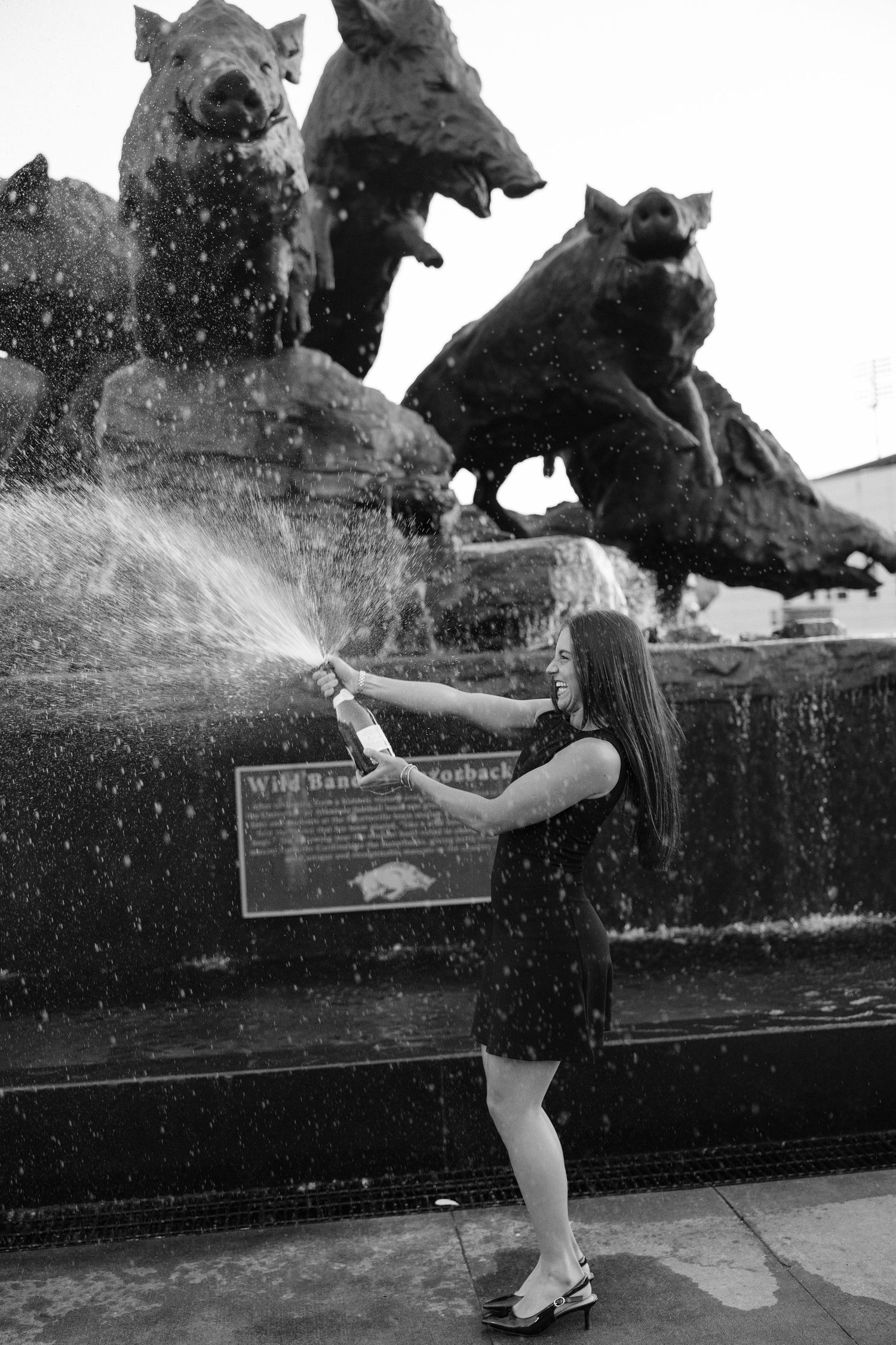 Young woman in black dress spraying water at Wild Hogs fountain sculpture in black and white photo.