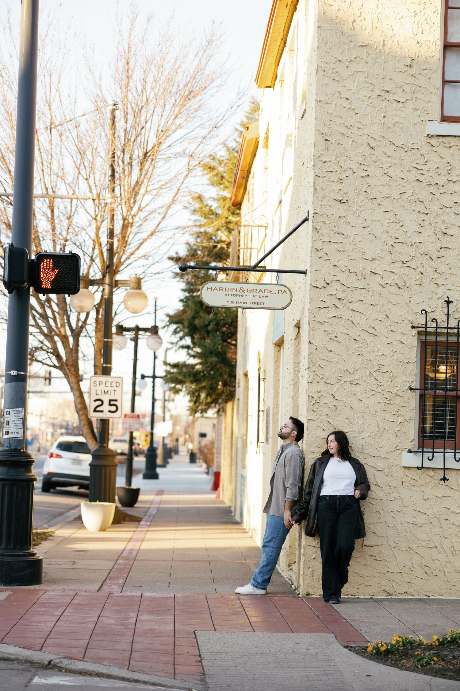 Couple standing together on a brick sidewalk next to a yellow building in a small town street corner.