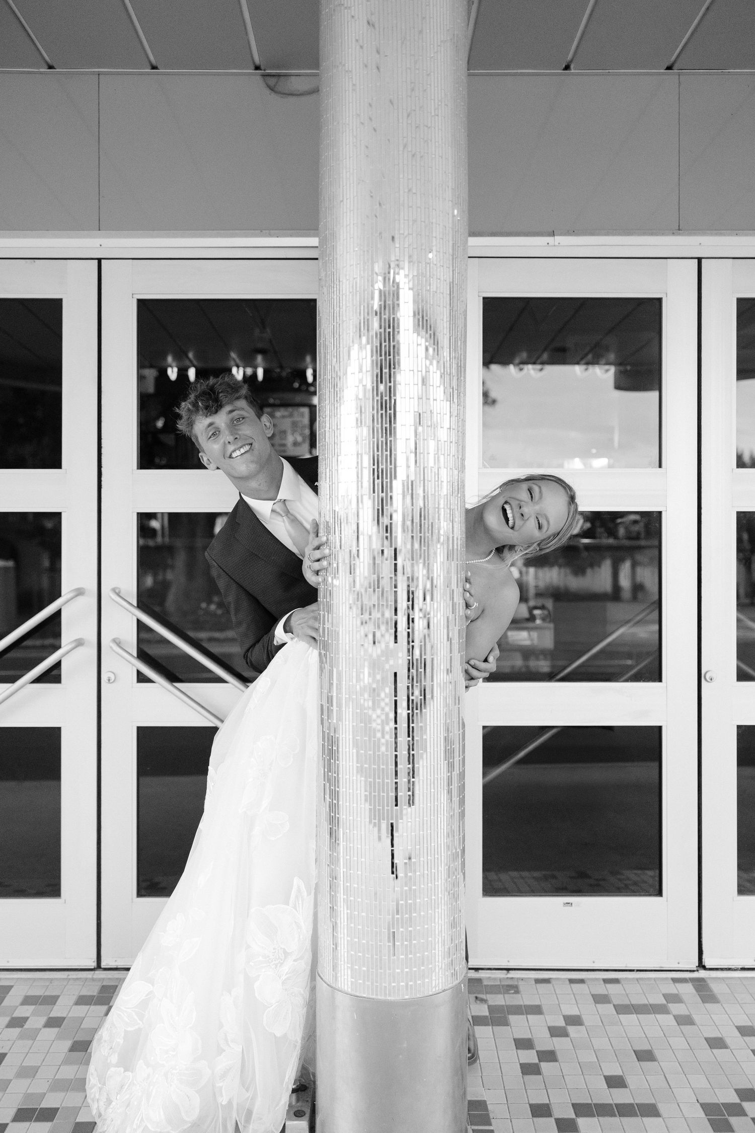 Bride and groom laughing around a glittery pillar in black and white wedding photo.