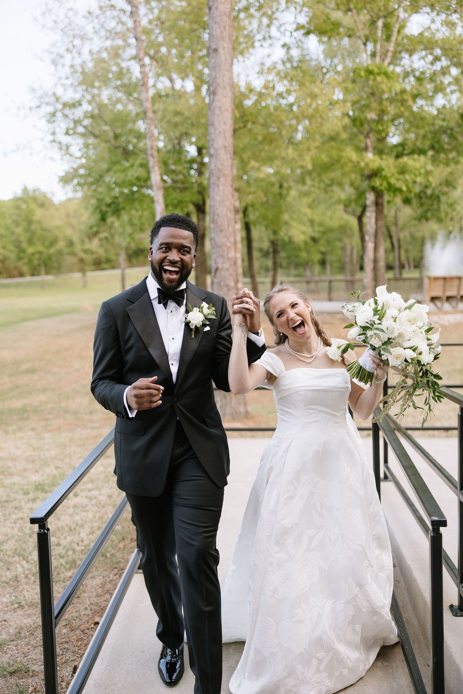 Joyful interracial newlyweds laughing while walking across bridge after ceremony.