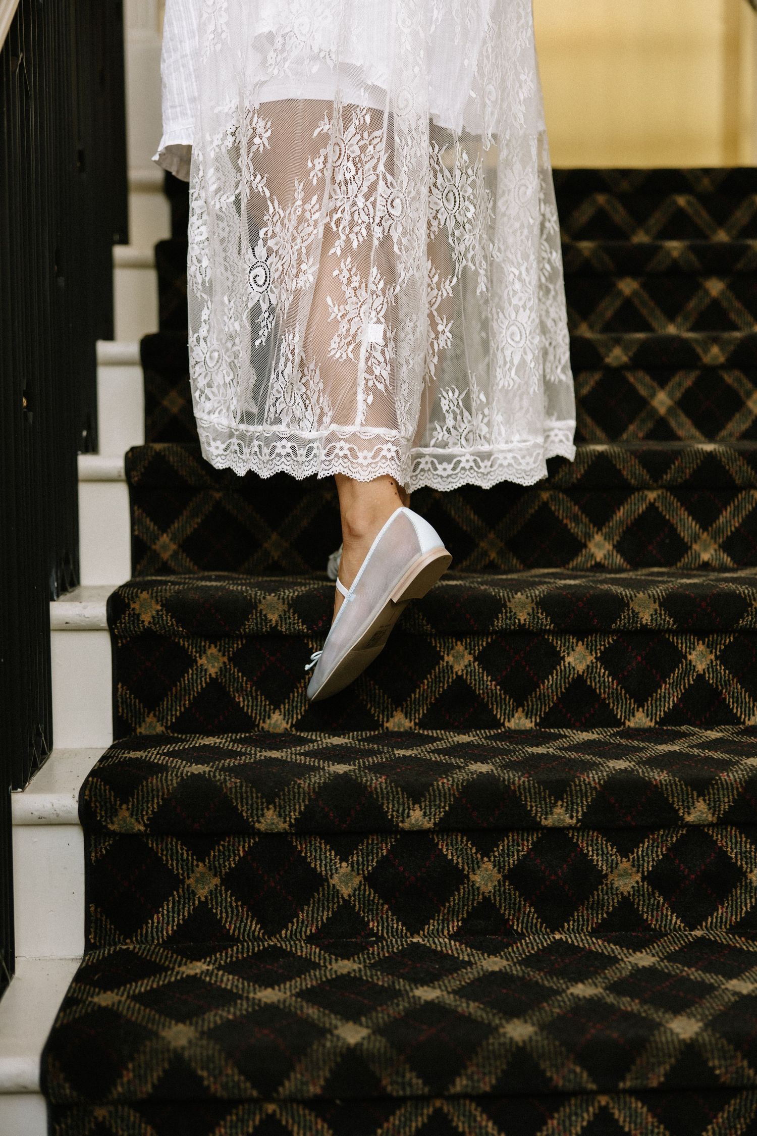 Close-up of a bride in lace wedding dress wearing white sneakers on a plaid-carpeted staircase.