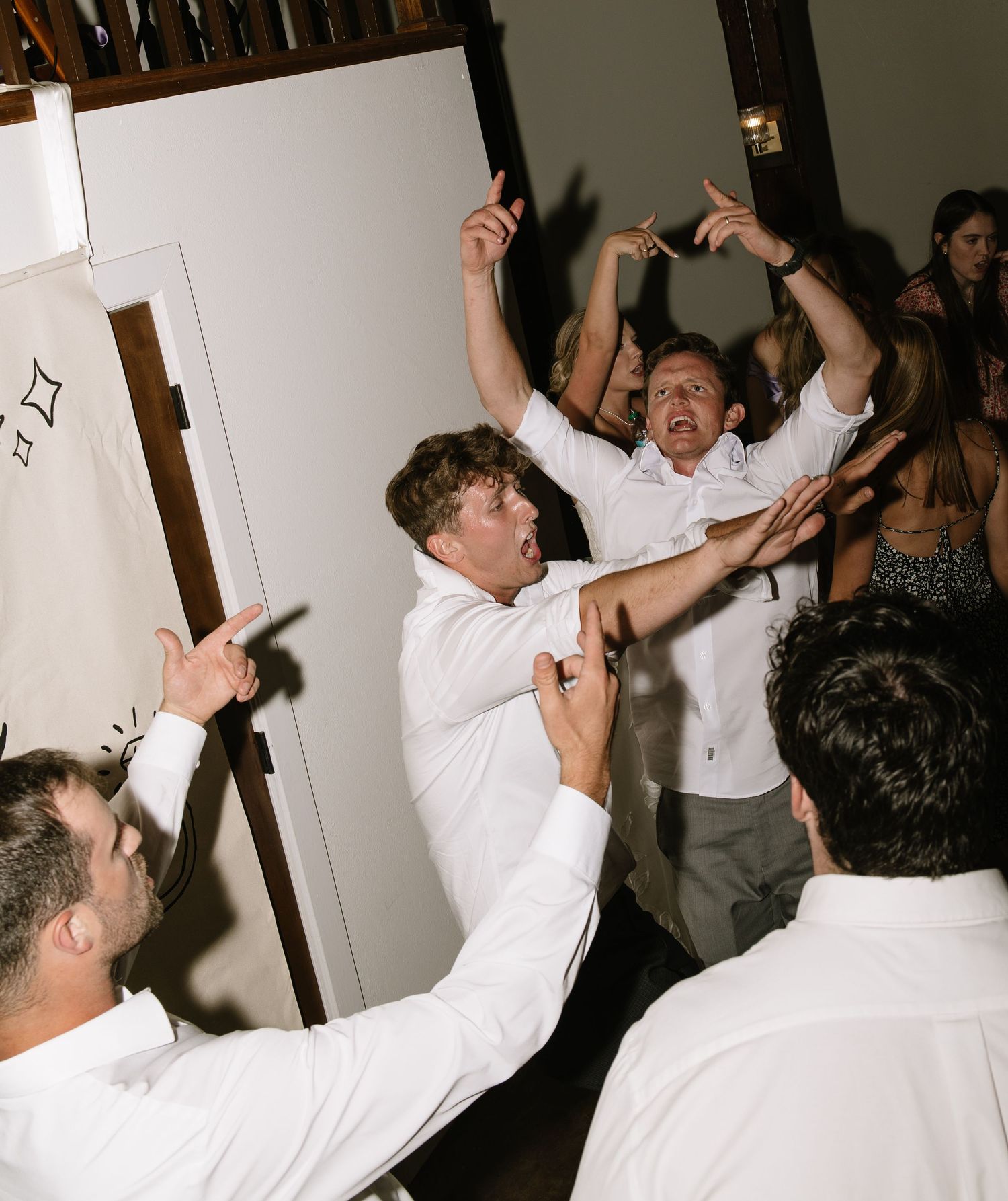 Groomsmen in white shirts celebrating energetically on the dance floor at a wedding reception.