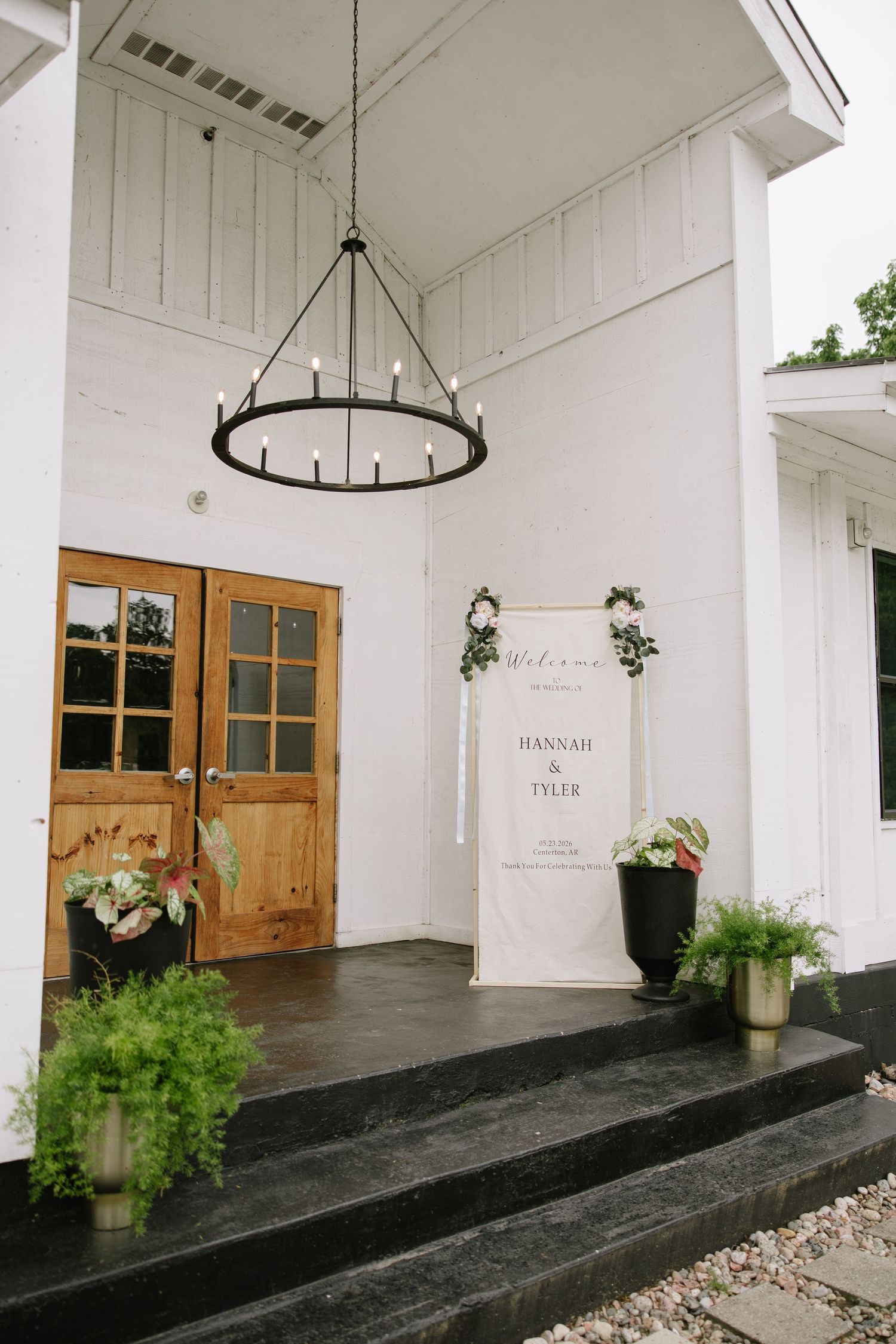 Elegant wedding welcome sign for Hannah & Tyler displayed at white venue entrance with wood doors and chandelier.