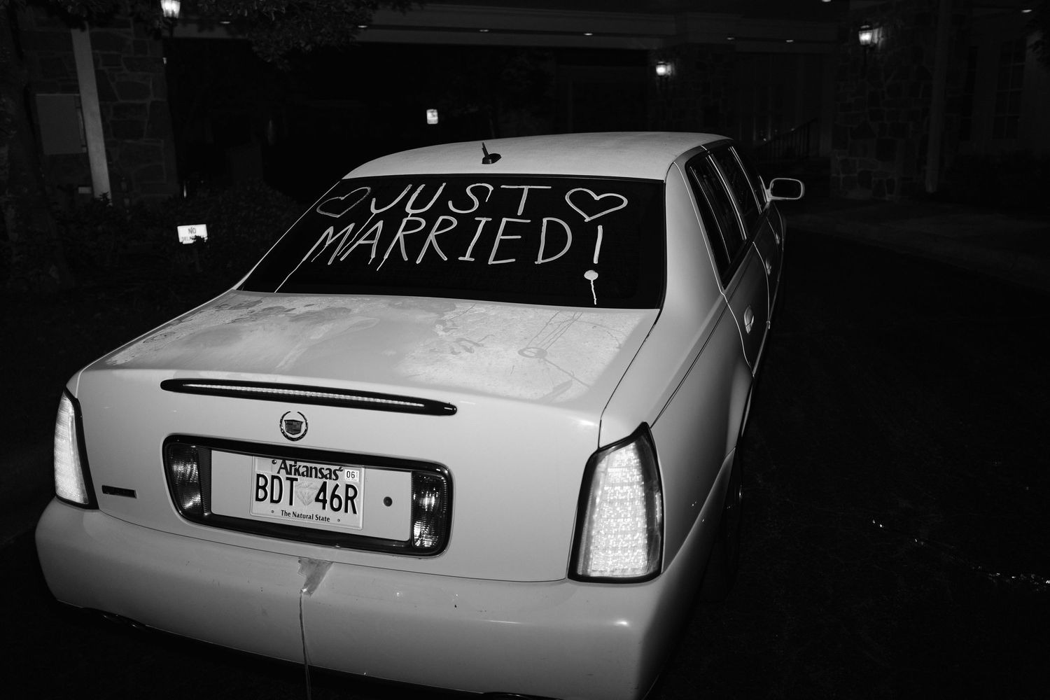 Black and white photo of white Cadillac with Just Married written on rear window at night.
