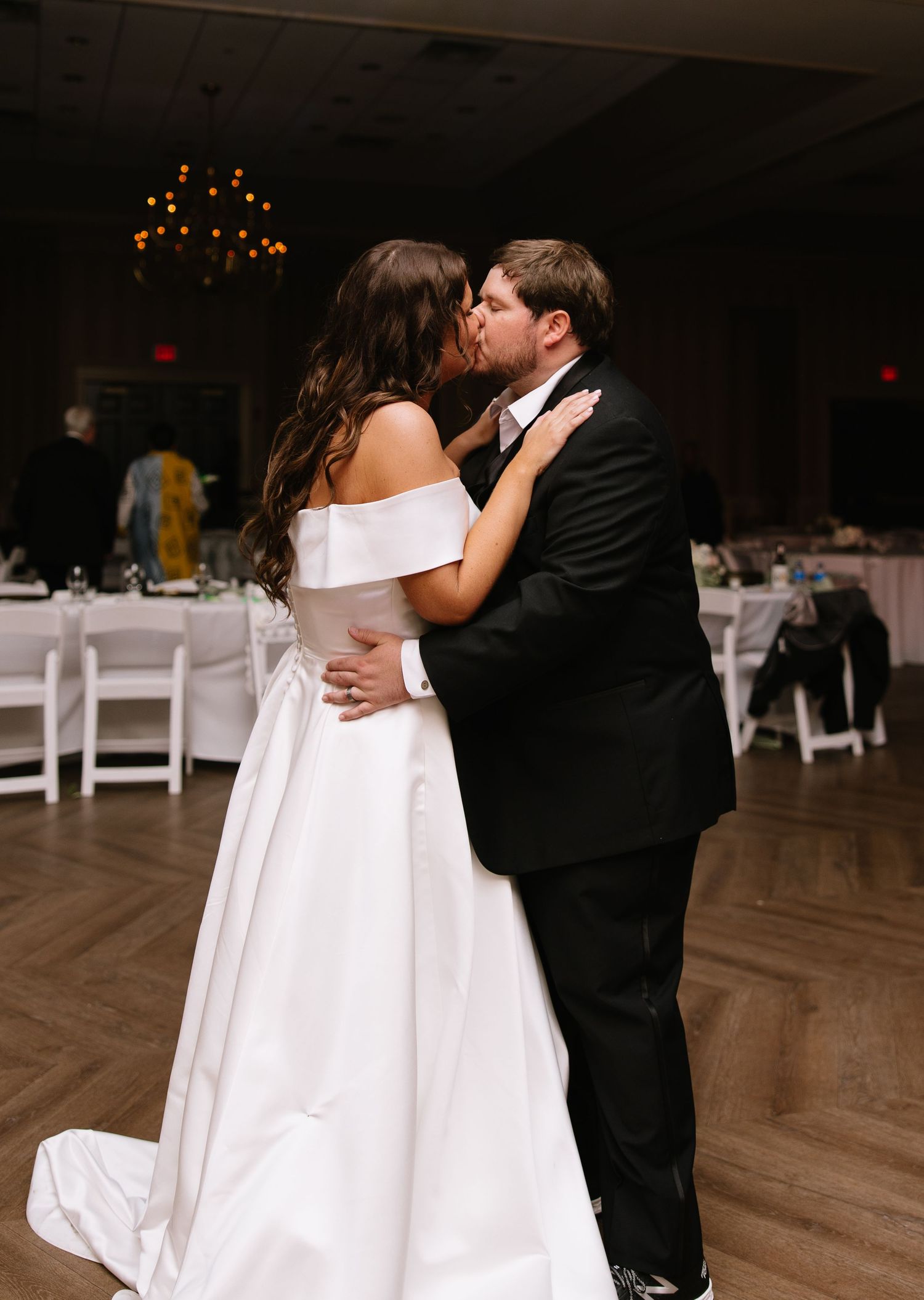 Bride and groom sharing first dance kiss in elegant reception hall wearing wedding attire.
