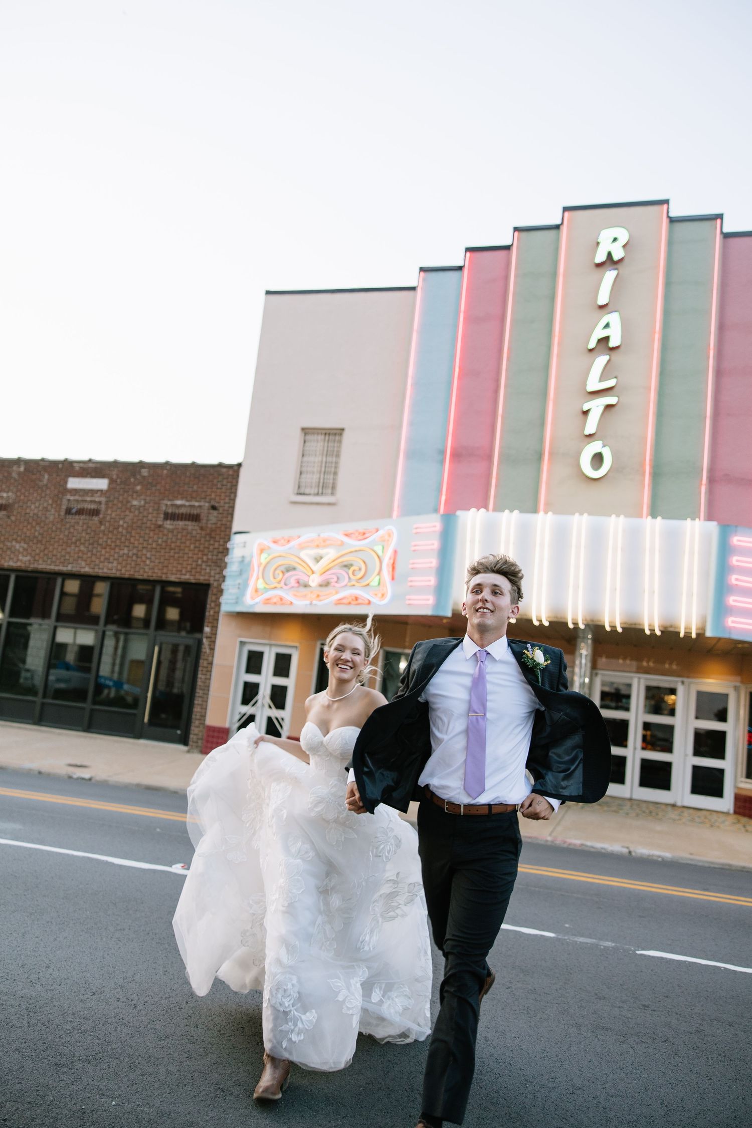 Bride and groom running joyfully in front of the Rialto Theater on their wedding day.