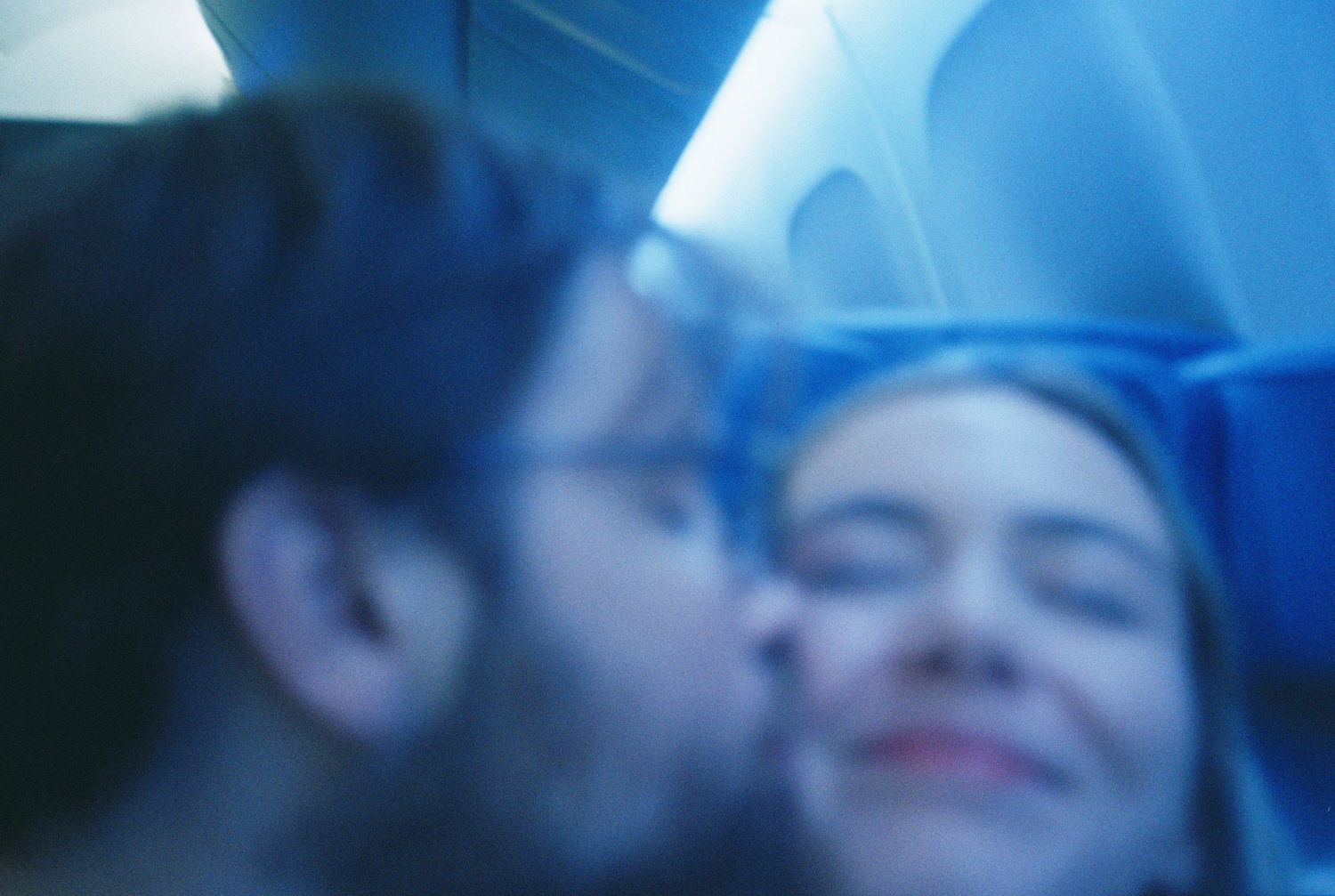 Blurry romantic film photo of couple kissing on an airplane with blue lighting.