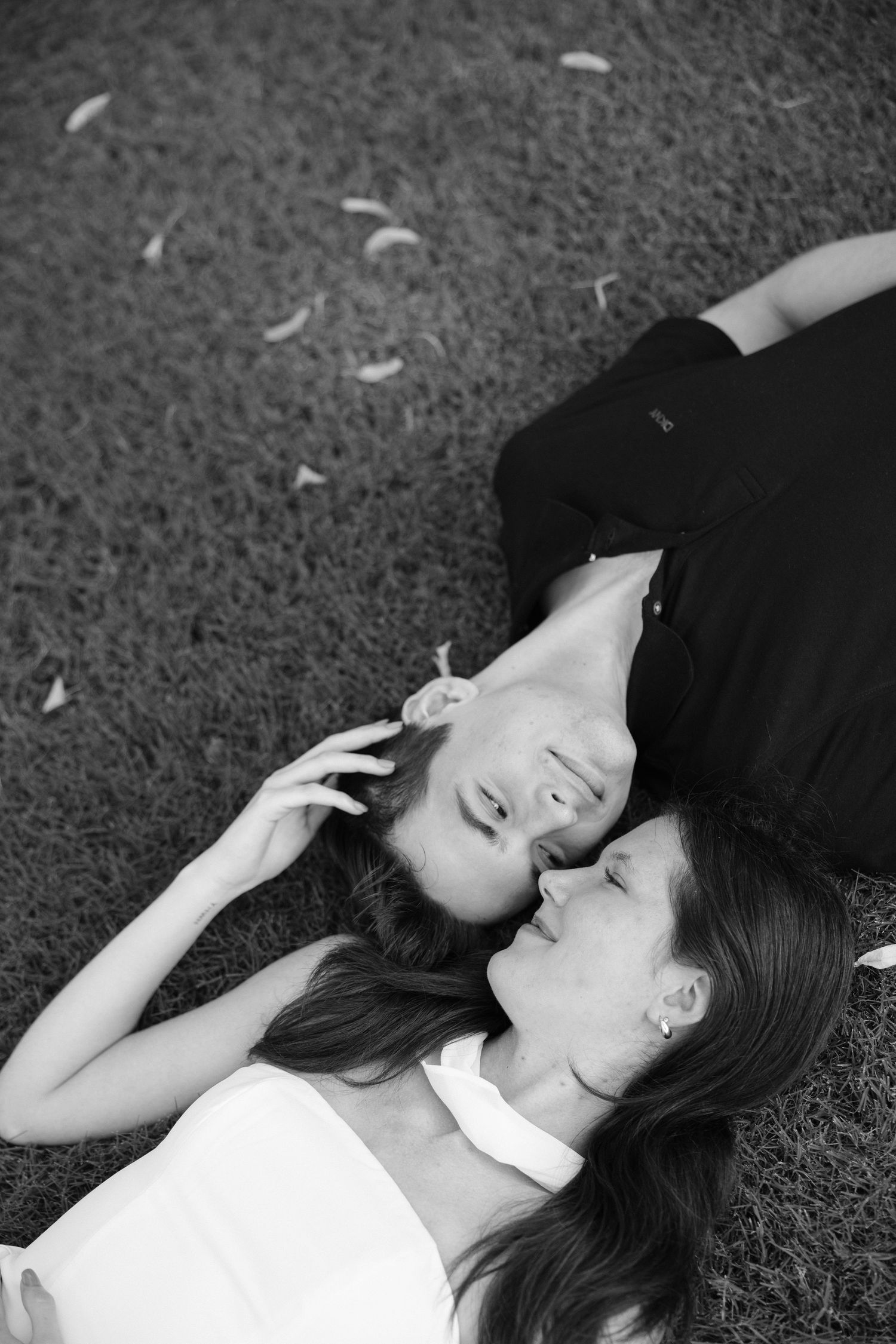 Black and white photo of two women lying on grass, facing each other in a tender, intimate moment.