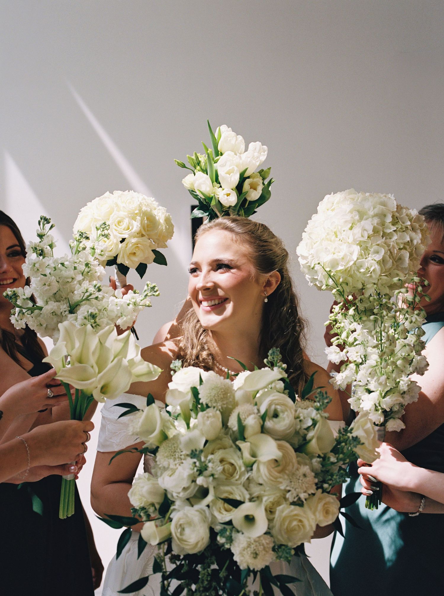 Bride surrounded by bridesmaids holding lush white floral bouquets at a wedding celebration.