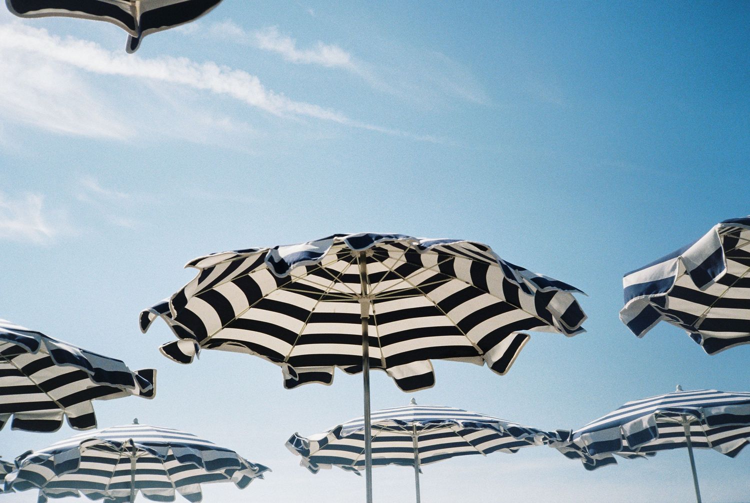 Black and white striped beach umbrellas against a bright blue sky at a seaside resort.