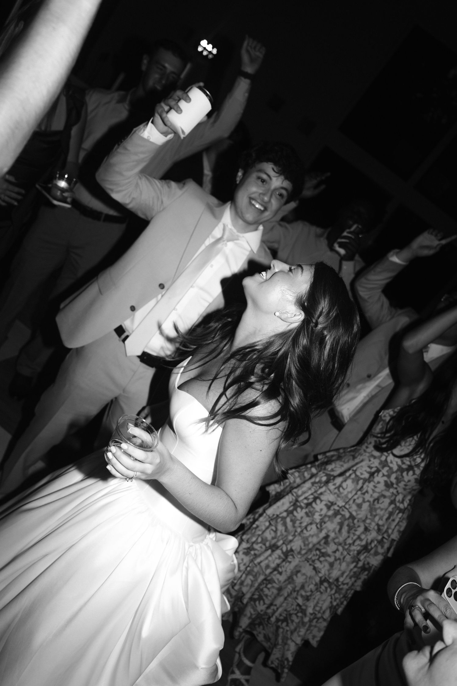 Black and white photo of a bride and groom dancing joyfully at their wedding reception party.