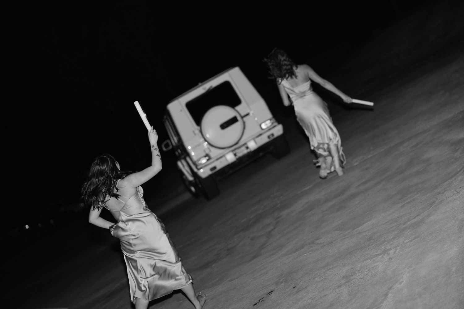Black and white photo of two flower girls waving goodbye as newlyweds depart in a white SUV at night.