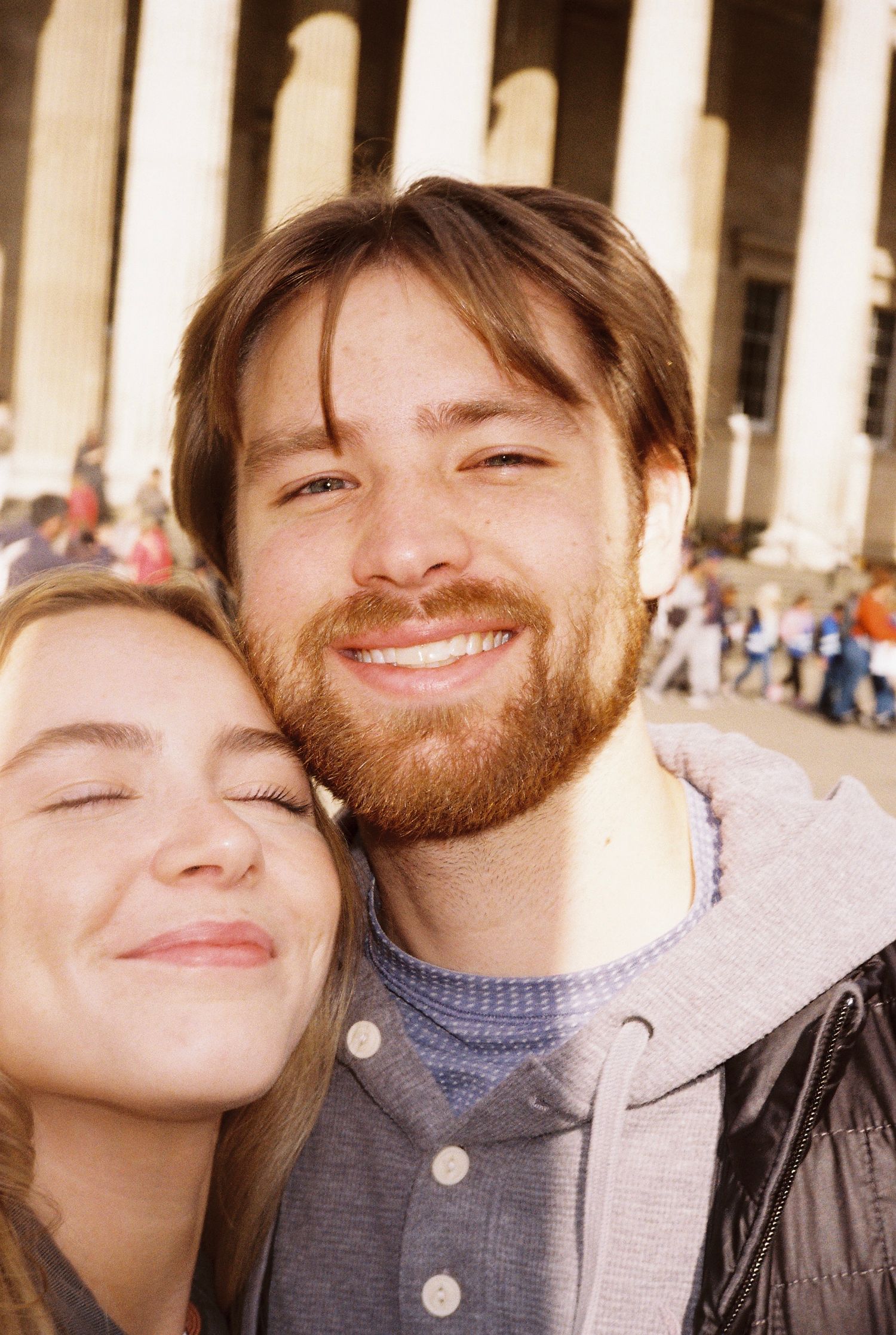 Smiling couple taking a selfie in front of large stone columns at a historic landmark.