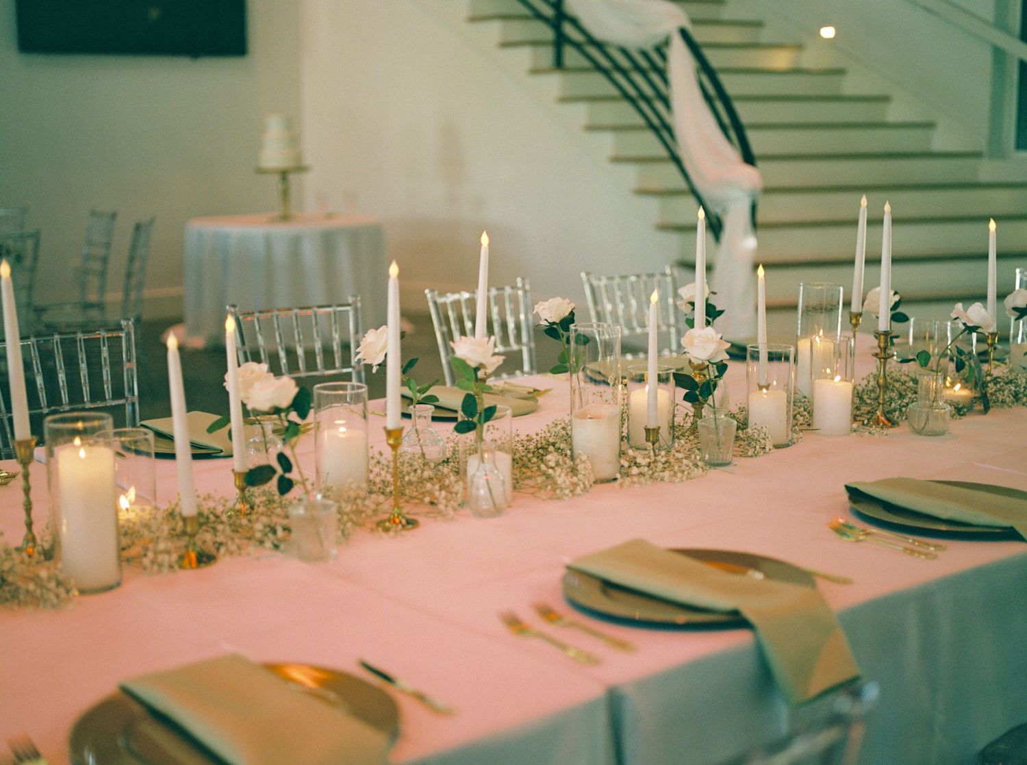 Elegant wedding reception table with white candles, gold accents, and floral centerpieces.
