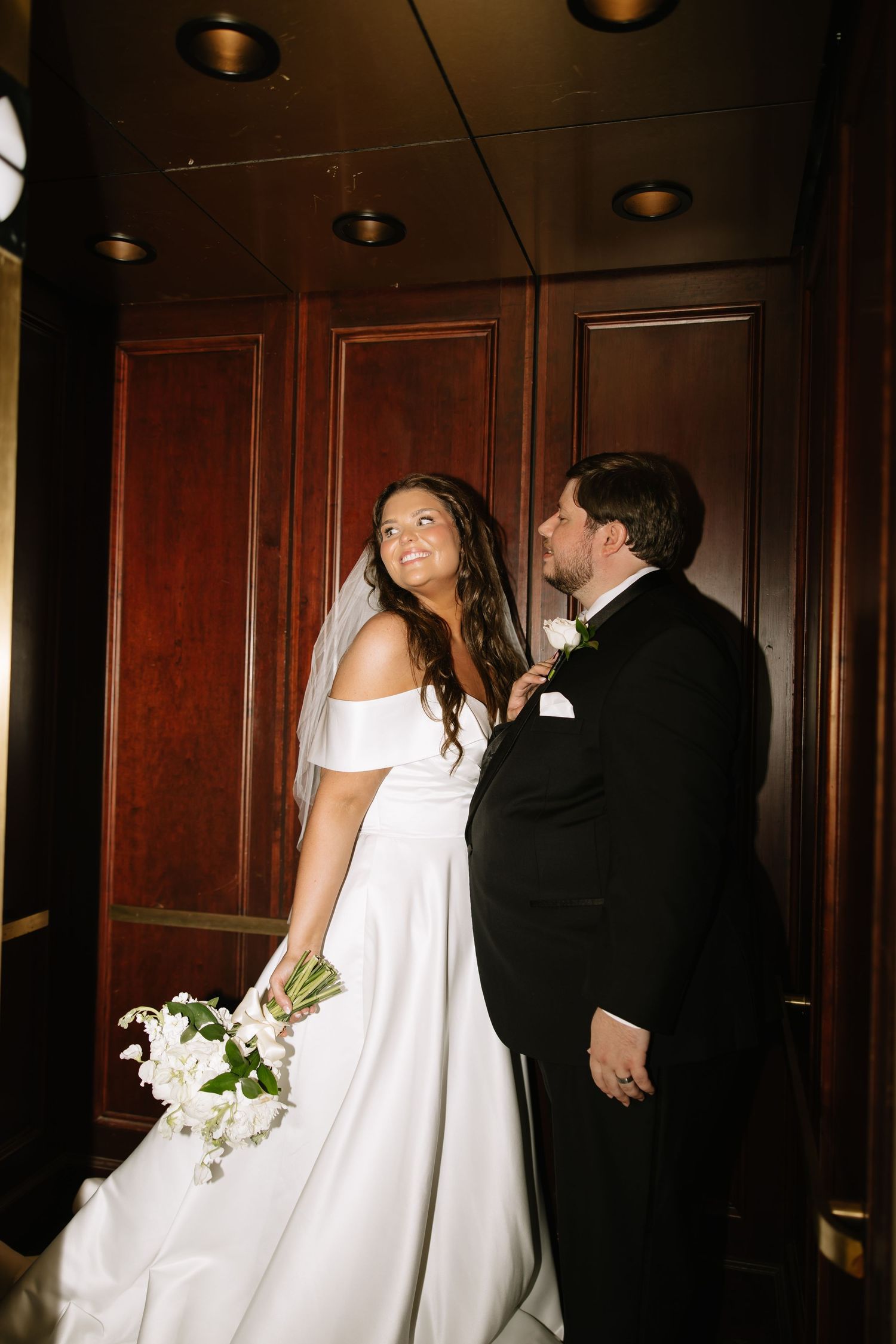 Bride and groom share romantic moment in elegant wood-paneled interior, bride holding white bouquet.