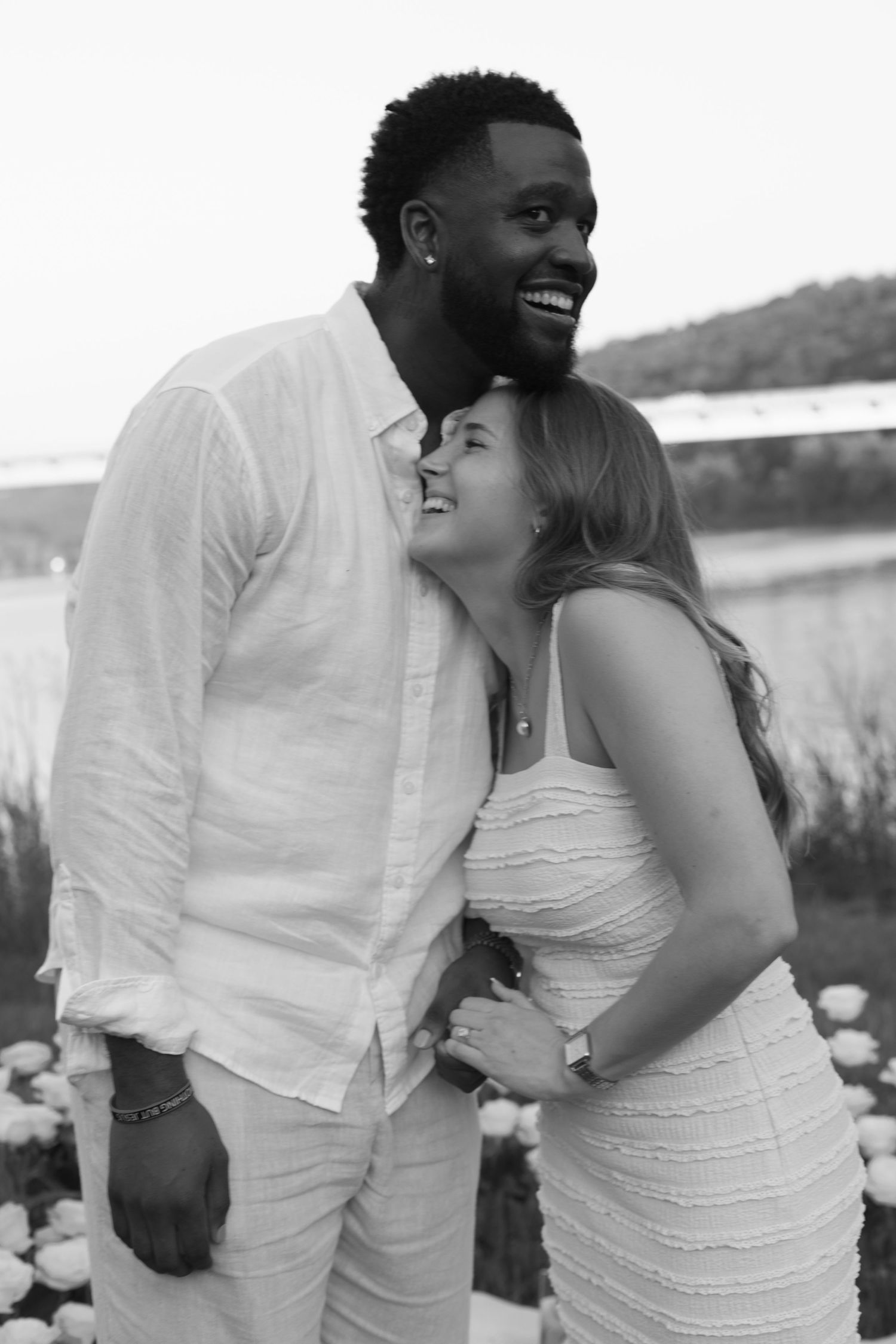 Happy interracial couple embracing and smiling outdoors near a river in black and white photo.
