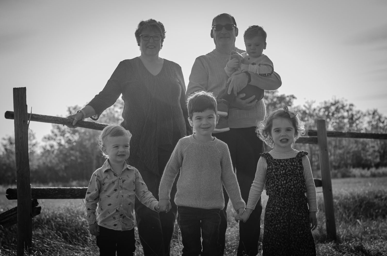 Black and white family photo of two women with four young children holding hands in a field.