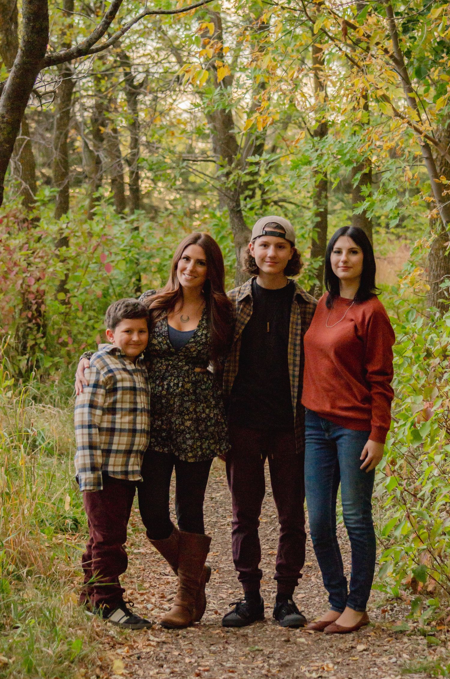 Family of four poses on a wooded trail surrounded by colorful autumn foliage for a fall portrait session.