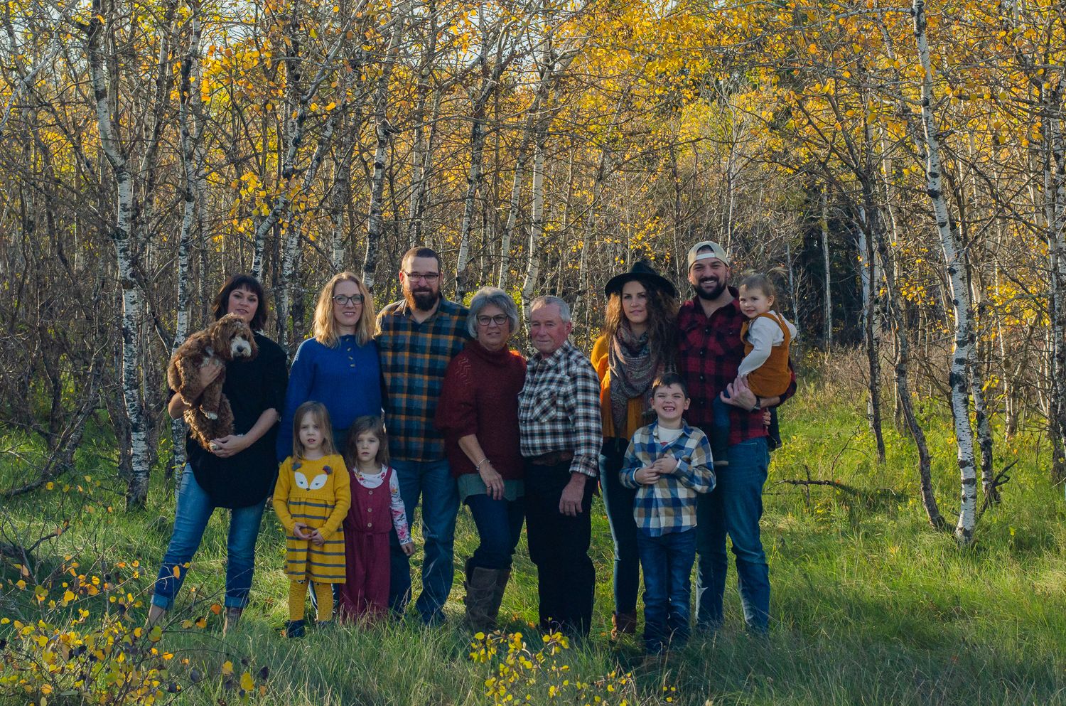 Large family group portrait outdoors among golden autumn birch trees in a meadow with wildflowers.