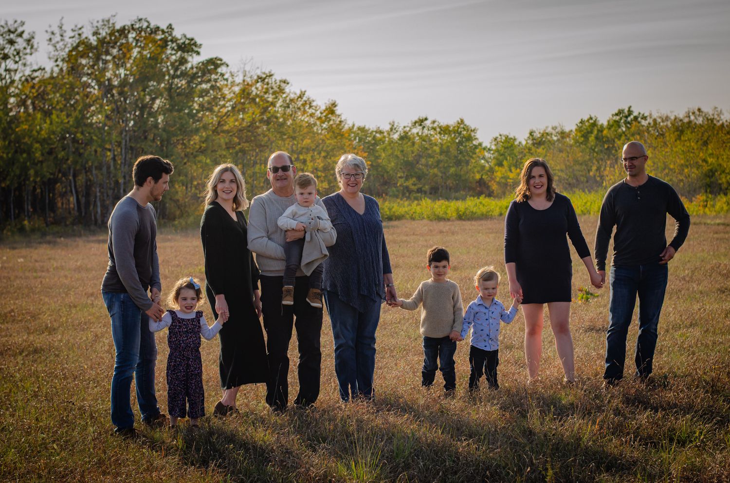 Multi-generational family portrait in golden field at sunset, eight members standing together outdoors.