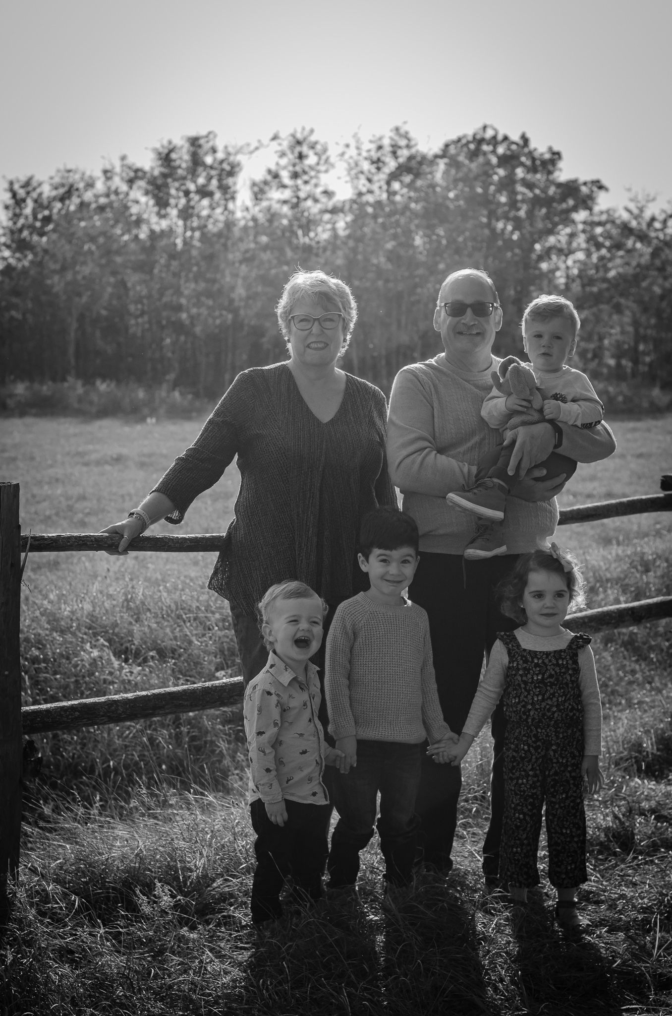 Black and white family photo of two adults and four children posing by a wooden fence in a rural field.
