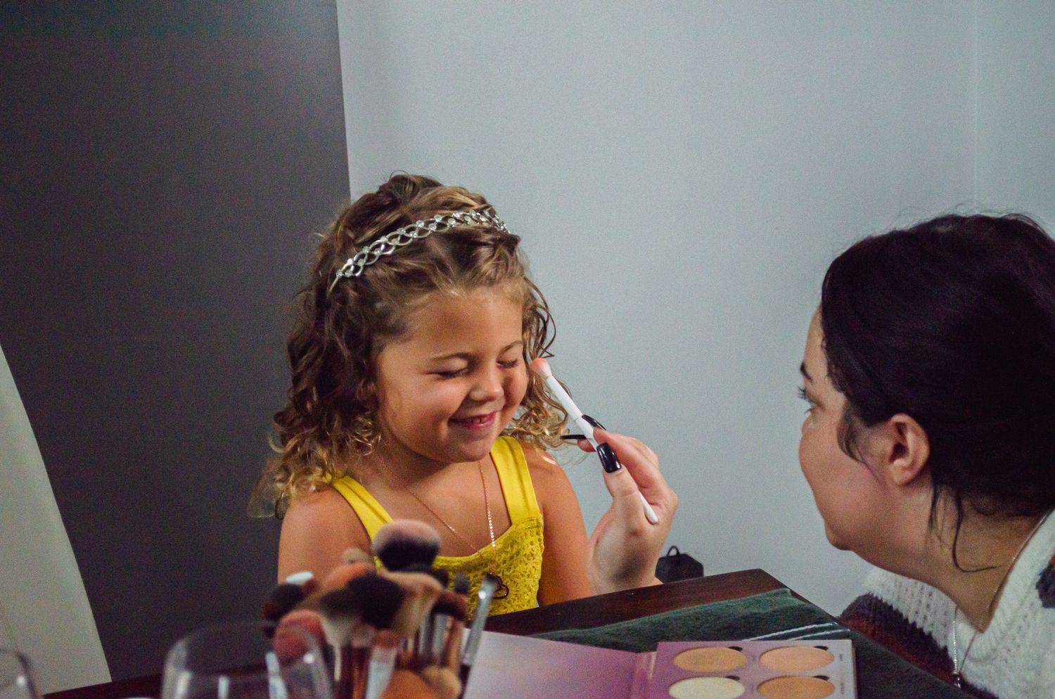 Young girl smiling as makeup artist applies cosmetics during a professional beauty session.