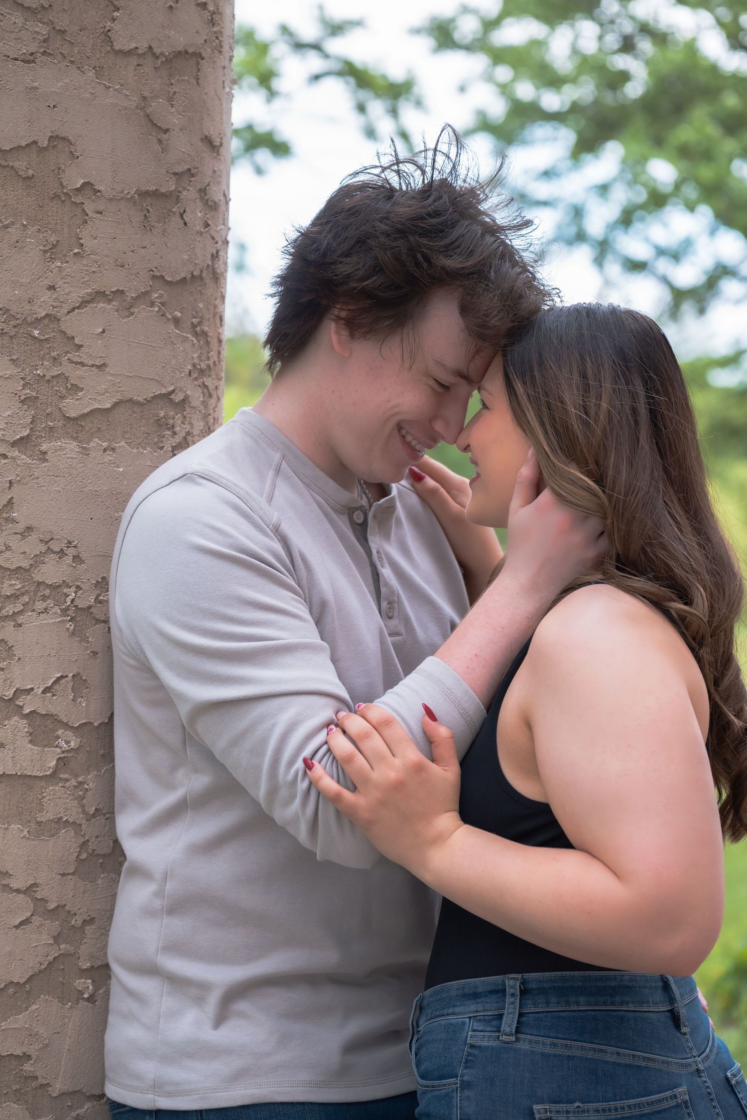 A young couple shares a romantic moment, touching foreheads and smiling outdoors near a textured wall.